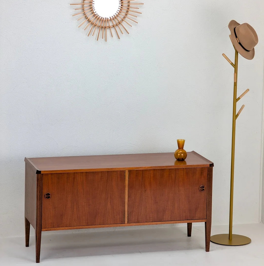 Mid-century modern wooden sideboard with sliding doors, amber glass vase, sunburst mirror and hat on brass coat rack