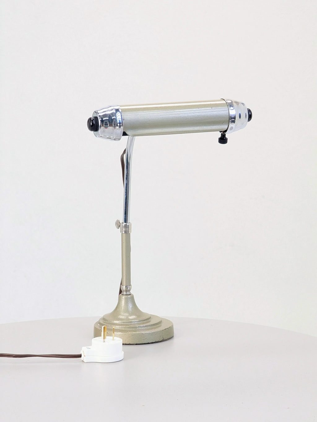 Vintage metal desk lamp with chrome accents on a round table, white plug visible