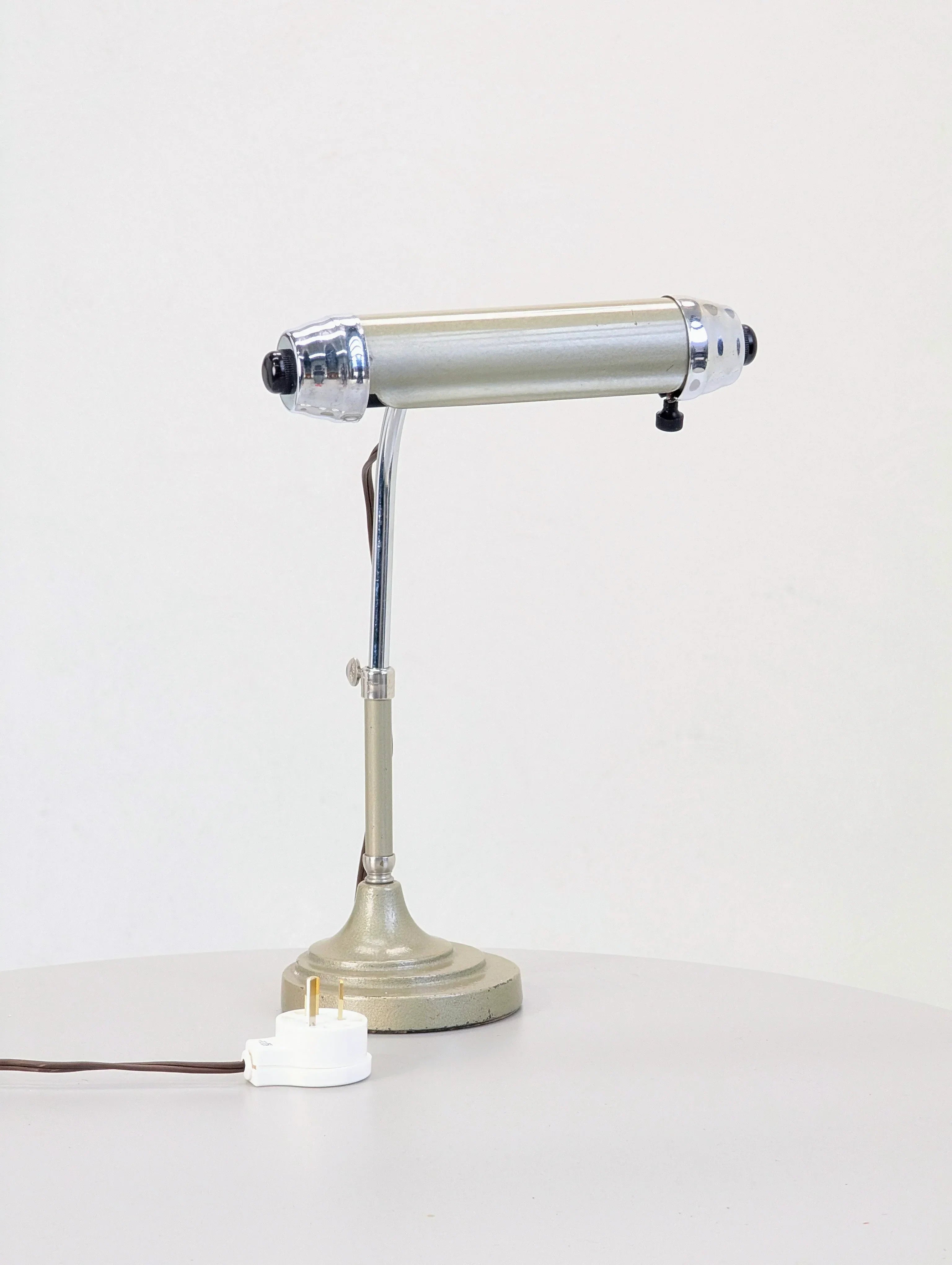 Vintage metal desk lamp with chrome accents on a round table, white plug visible