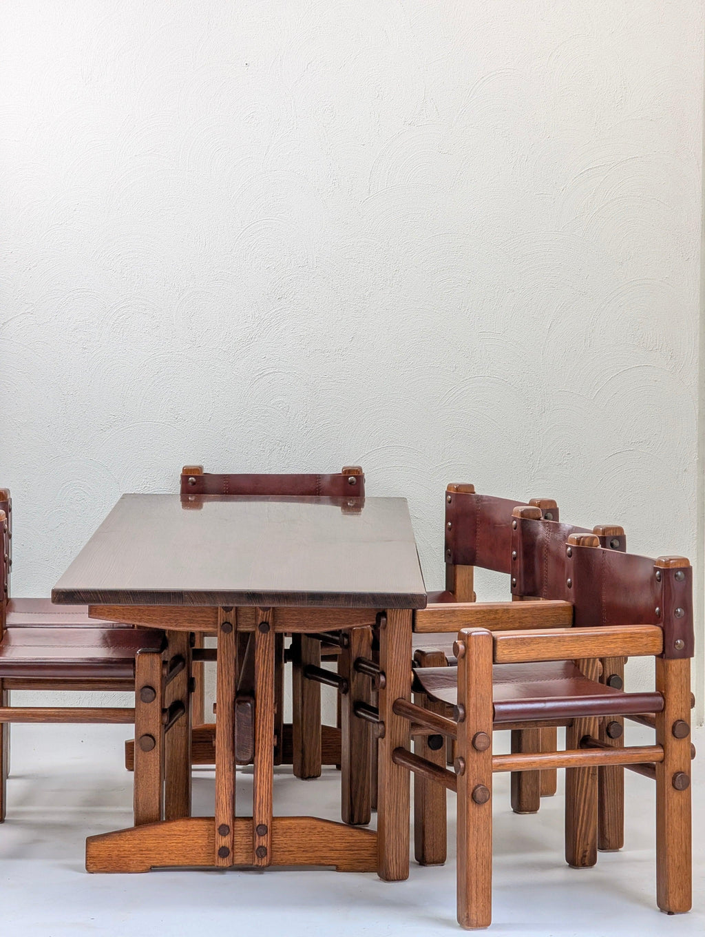Vintage wooden dining table set with four leather and wood chairs against a white wall