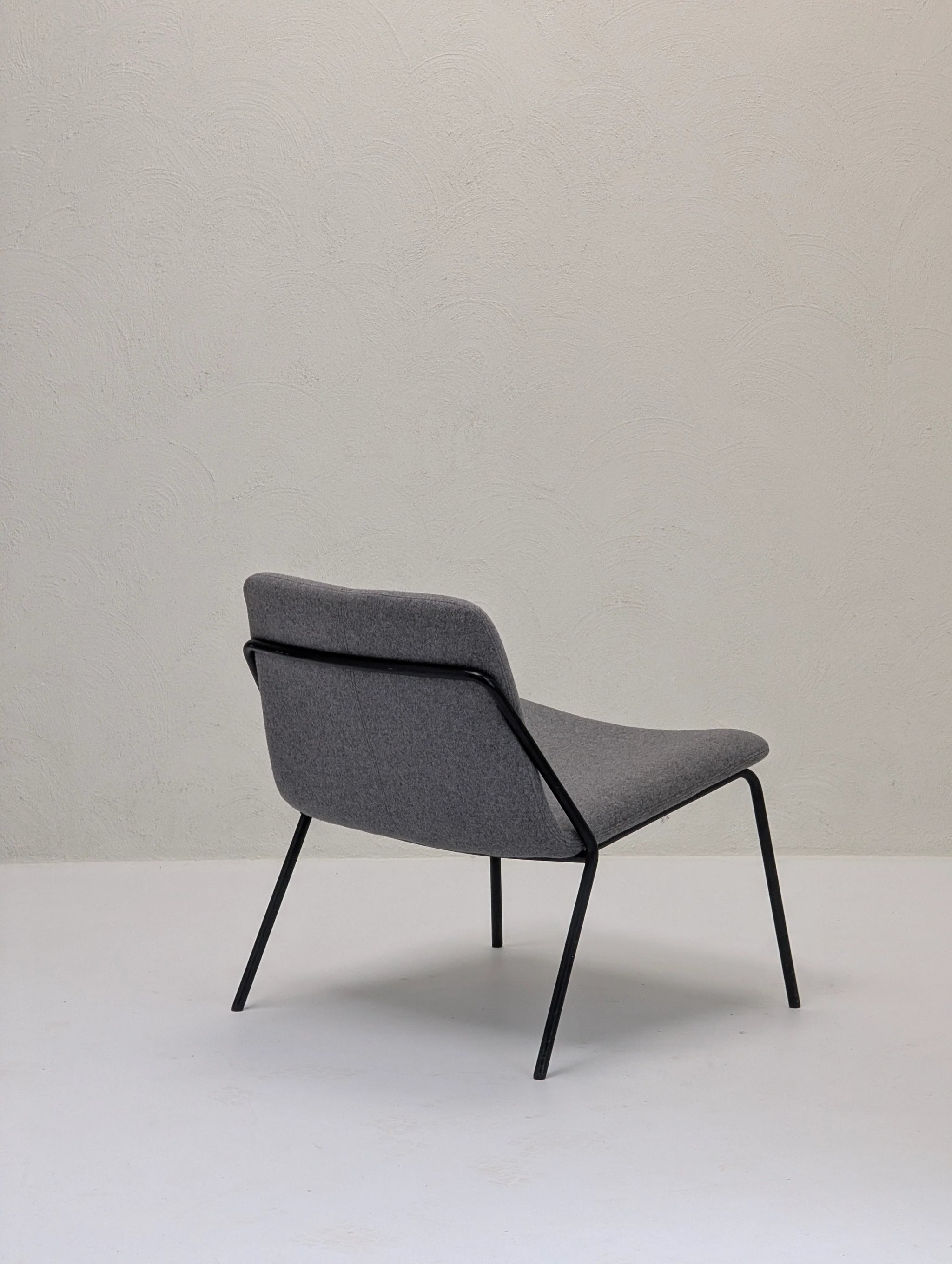 Modern gray upholstered lounge chair with black metal legs on white floor against textured wall
