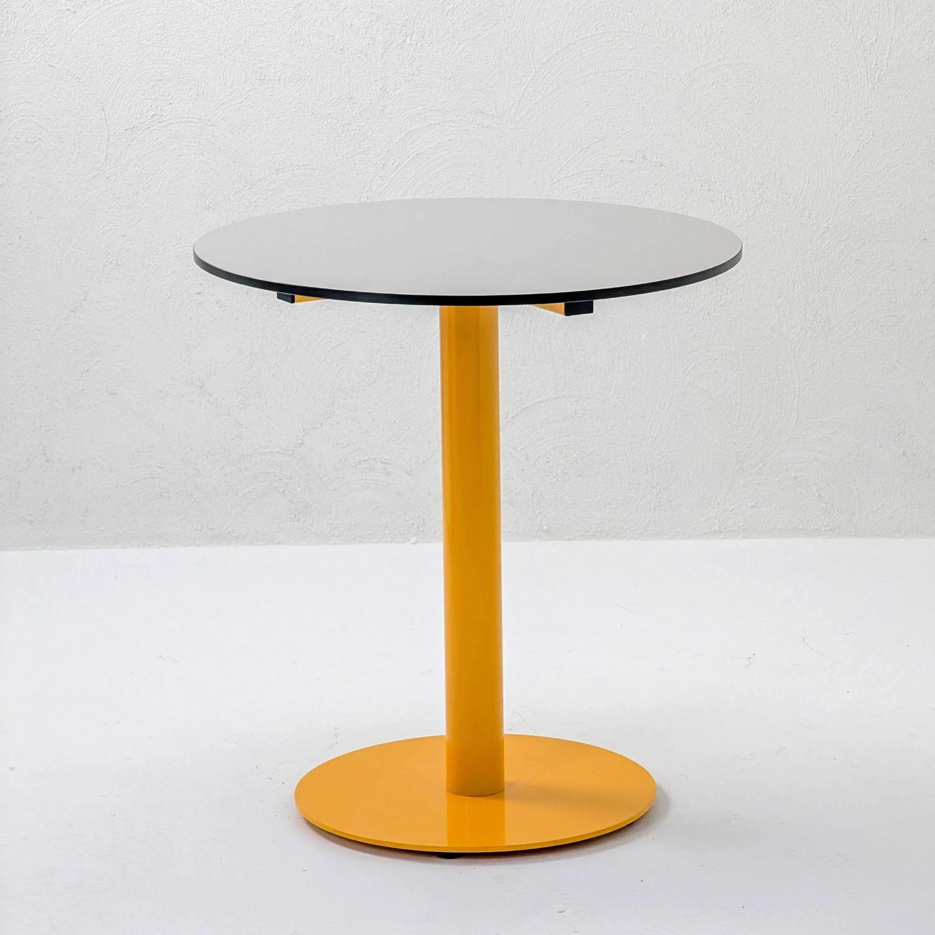 Modern round table with white top and yellow metal base against a white textured wall