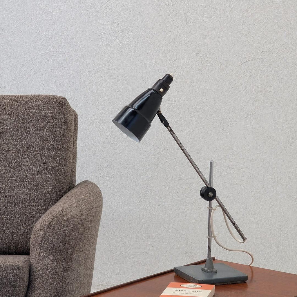 Vintage black adjustable desk lamp on wooden table beside gray upholstered chair