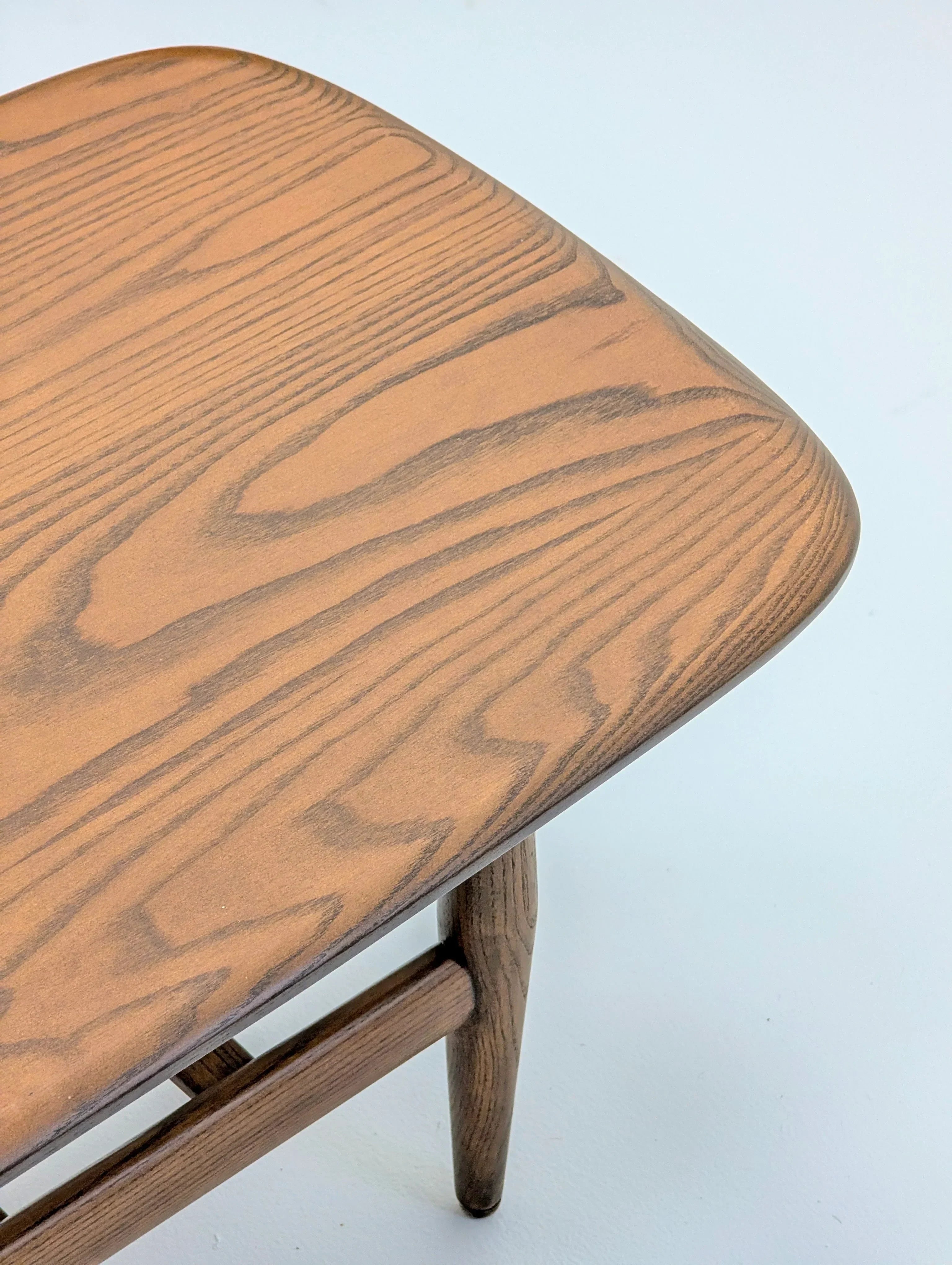 Close-up of a wooden chair seat with visible grain and smooth finish on a light background