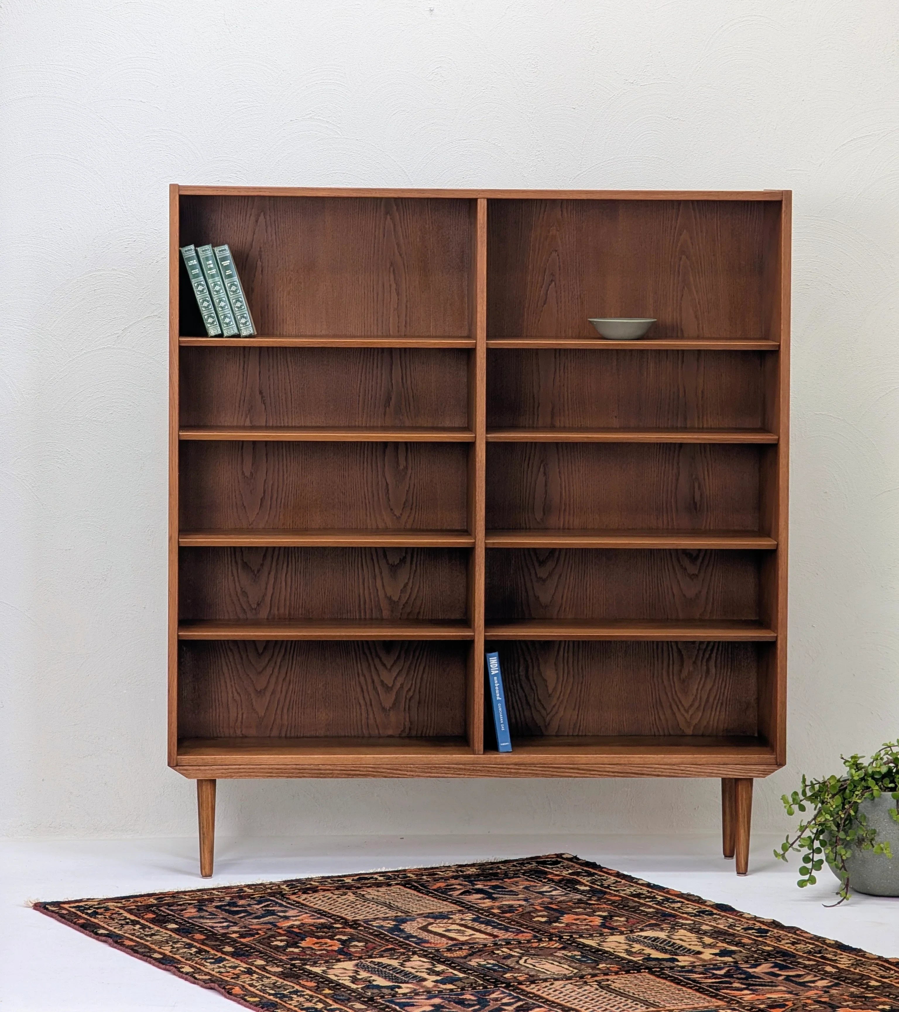 Mid-century modern wooden bookshelf with few books, decorative bowl, patterned rug, and potted plant