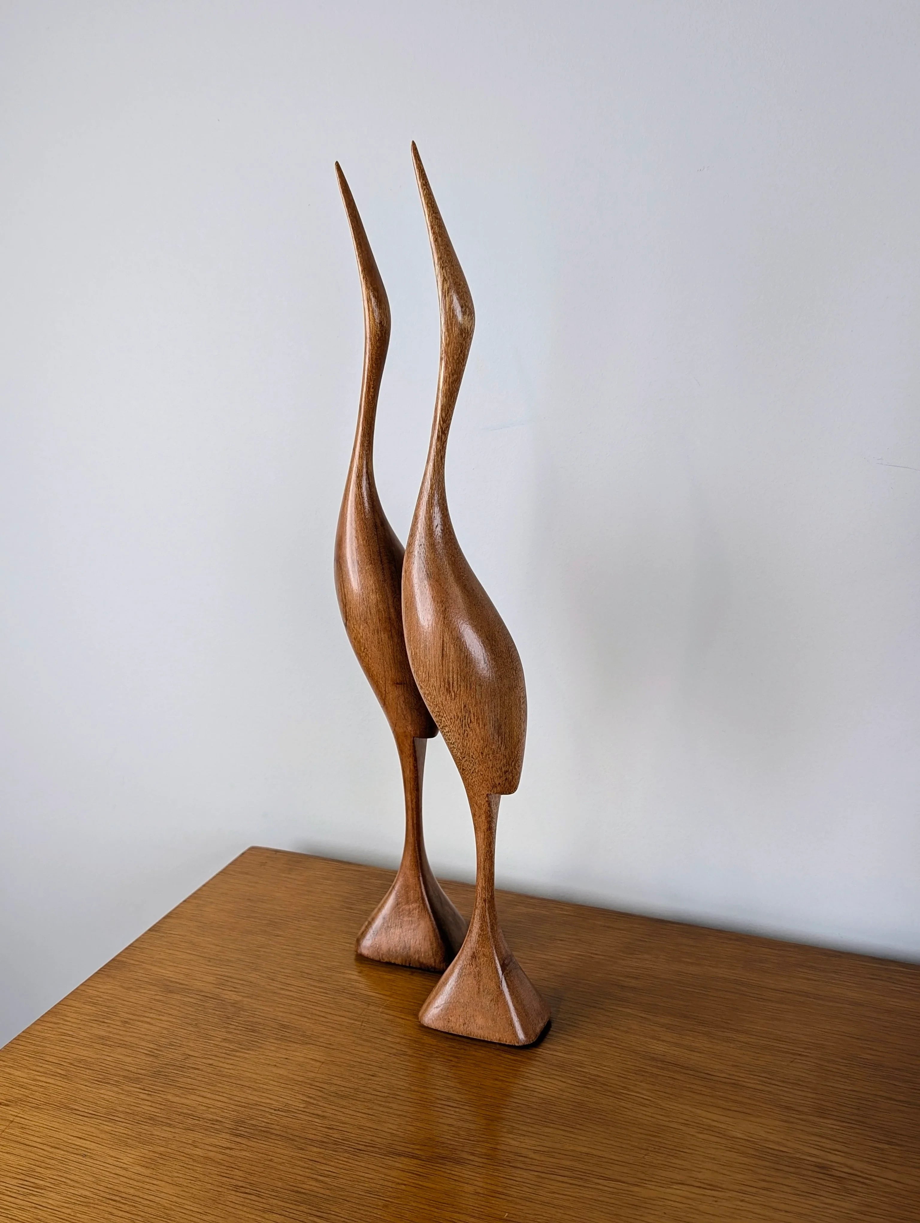 Pair of carved wooden crane bird sculptures on a wooden table against a plain wall