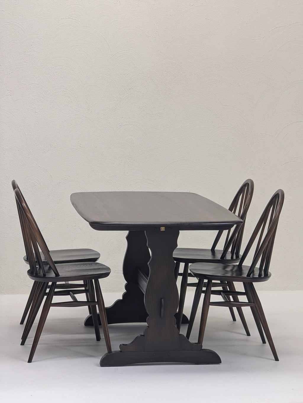 Dark wooden dining table with carved pedestal base and four matching chairs in minimalist setting