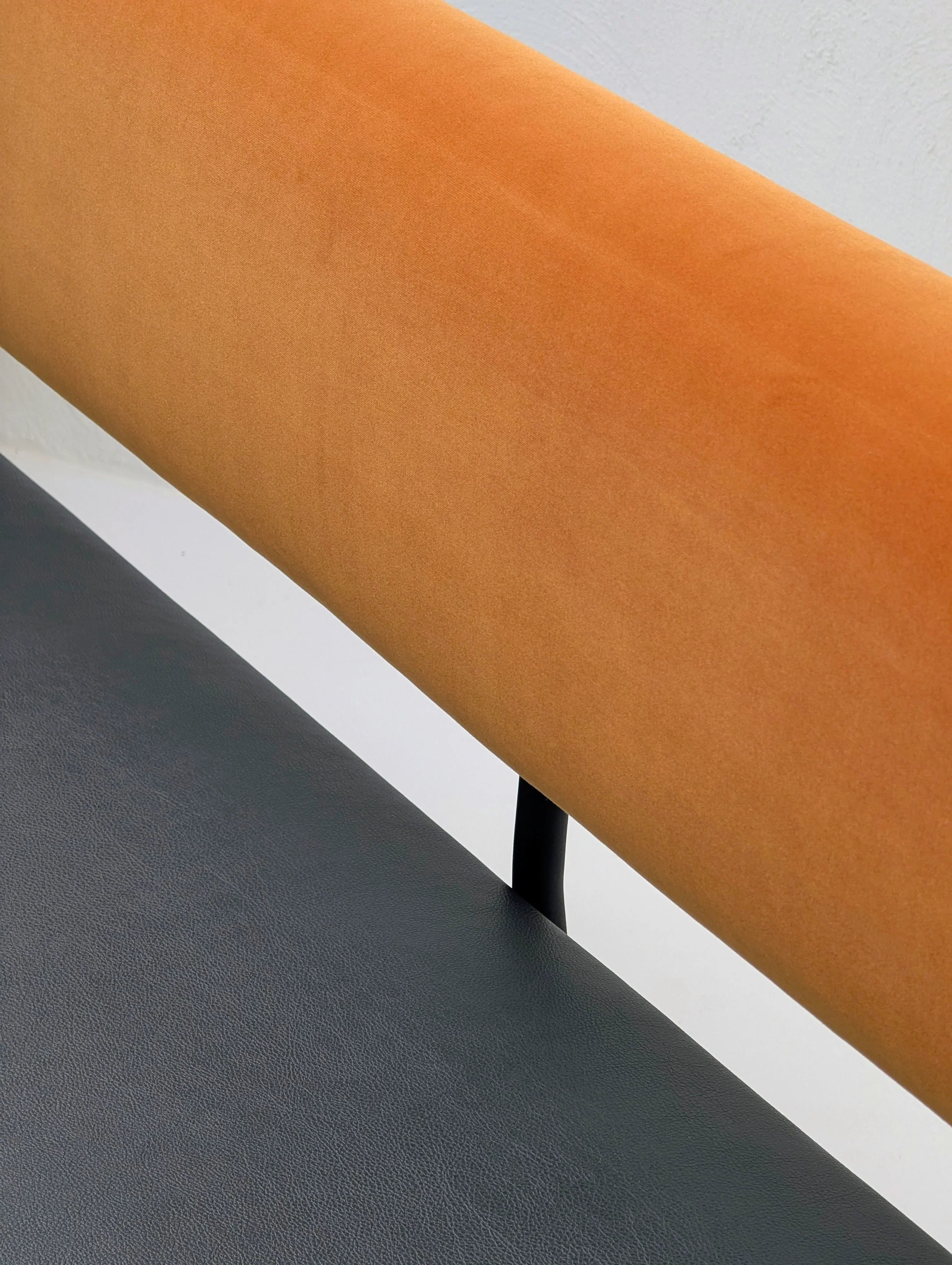 Modern chair with orange fabric backrest and black leather seat, minimalist design
