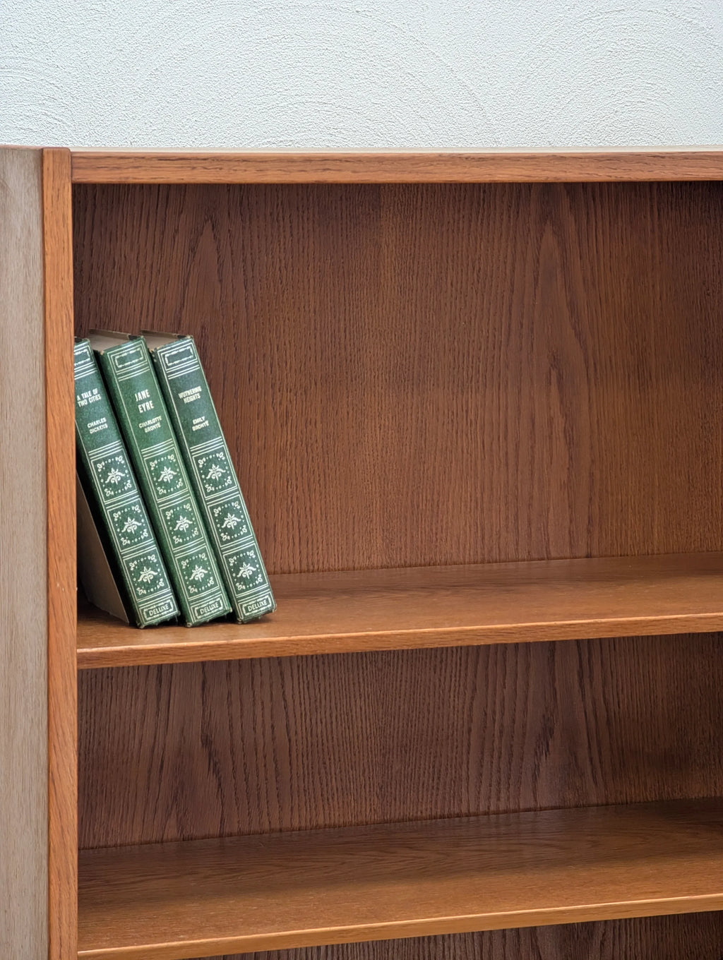 Wooden bookshelf with three vintage green hardcover classic novels on the middle shelf