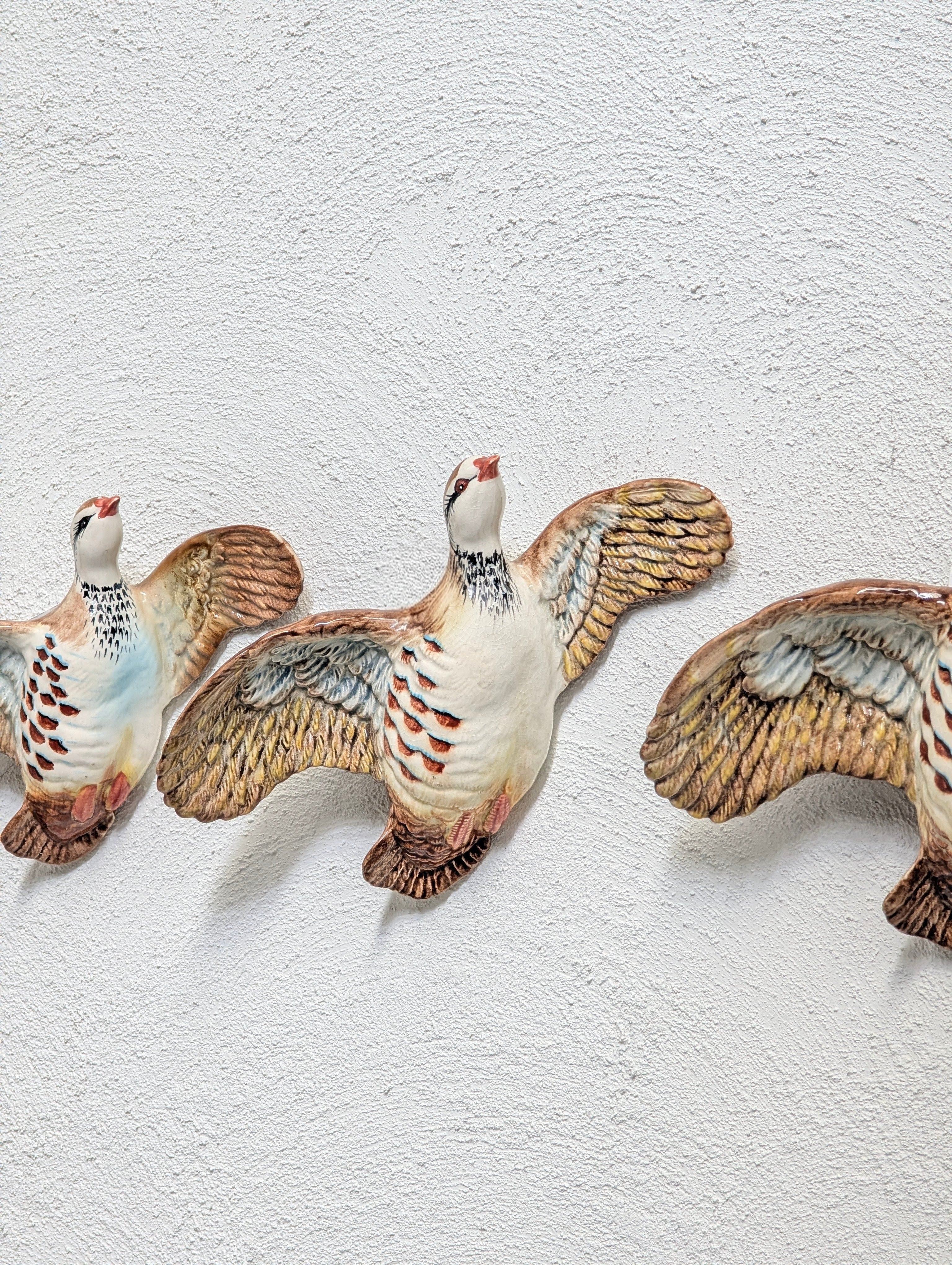 Three ceramic bird wall decorations with outstretched wings on a textured white wall