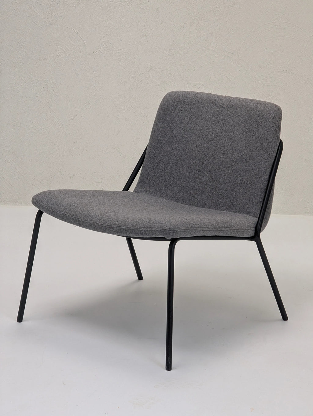 Modern gray lounge chair with black metal legs on a white floor and textured white wall background