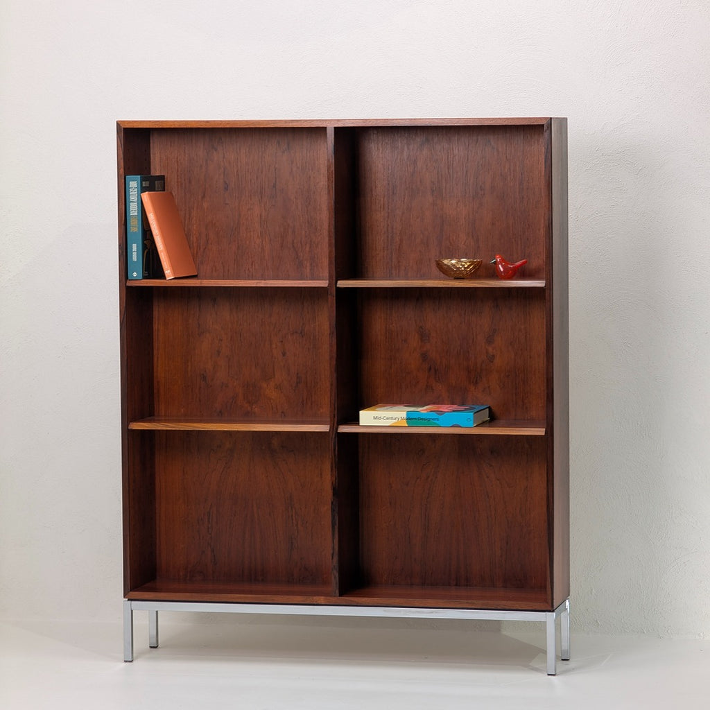 Mid-century modern wooden bookshelf with chrome legs, holding books and decorative items