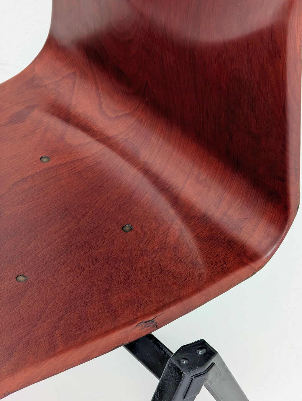 Close-up of vintage mid-century modern wooden chair seat with smooth reddish-brown finish and black metal legs