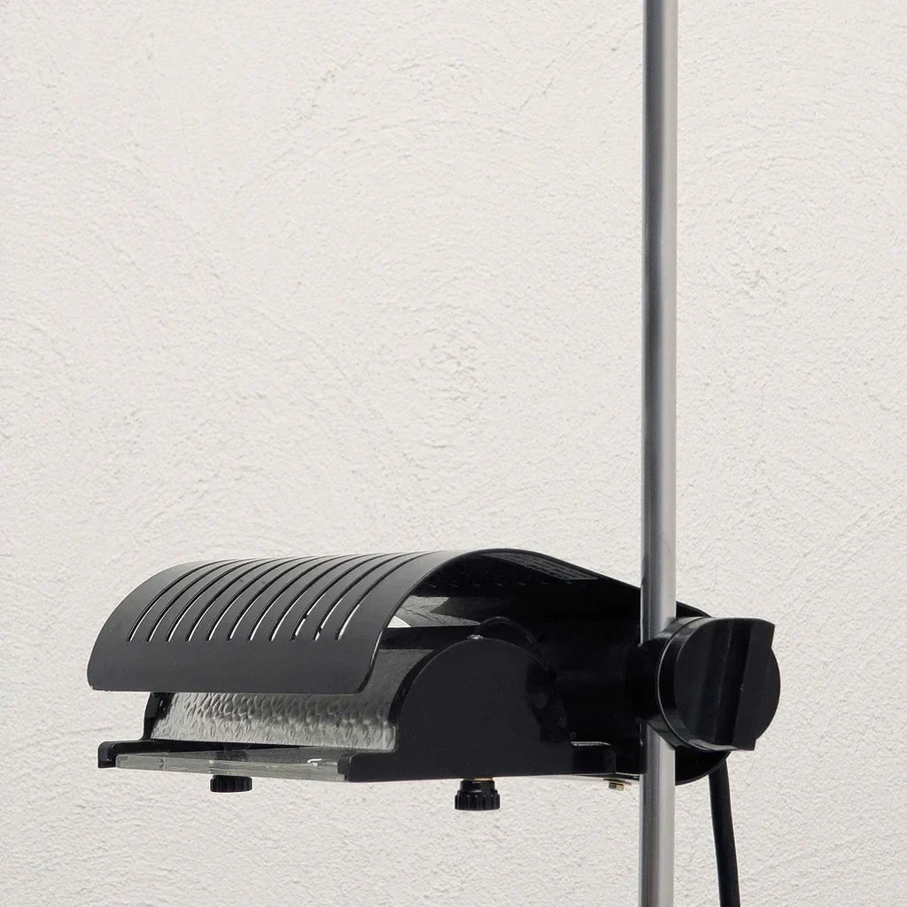 Black adjustable floor lamp head with vented cover on a metal pole against white wall