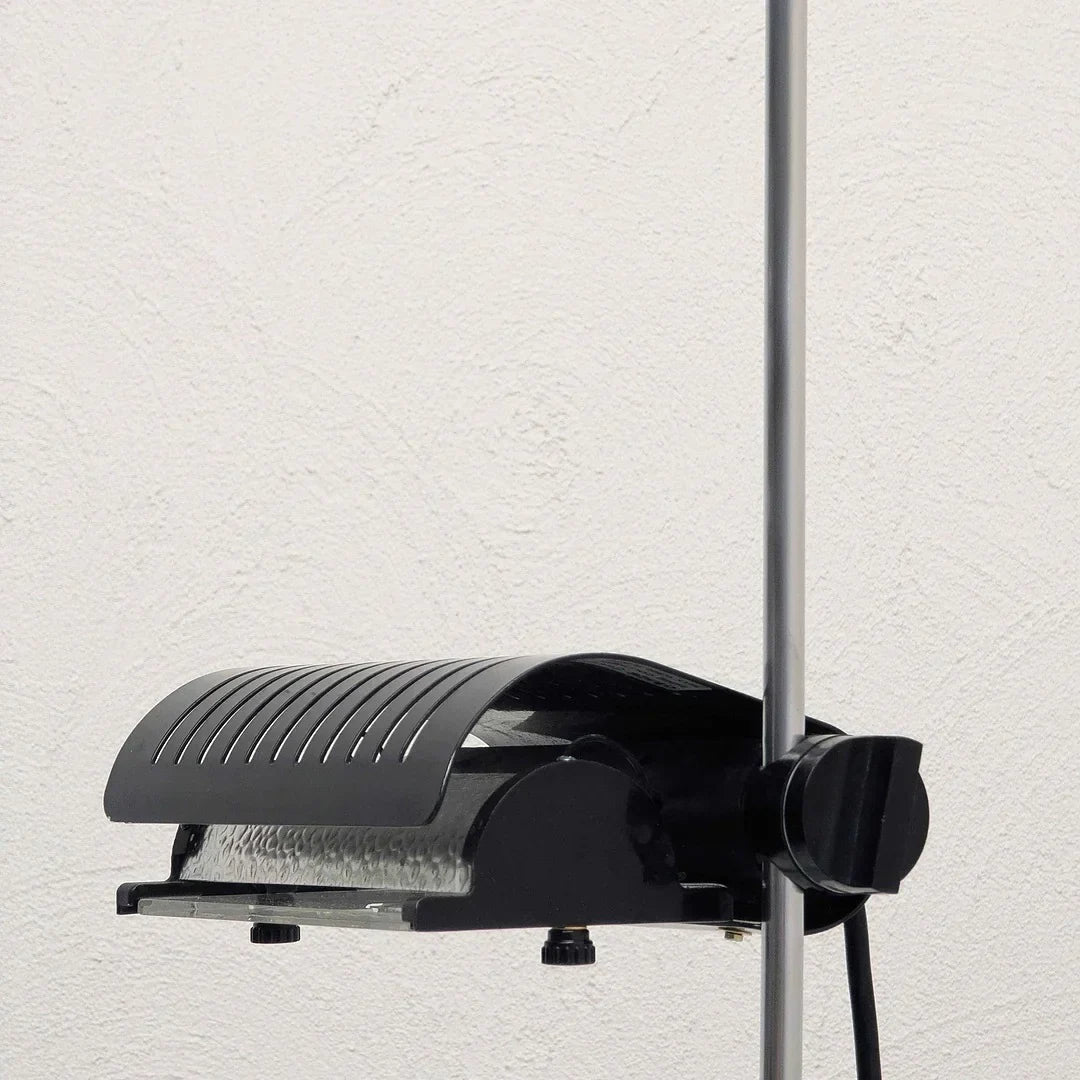 Black adjustable floor lamp head with vented cover on a metal pole against white wall