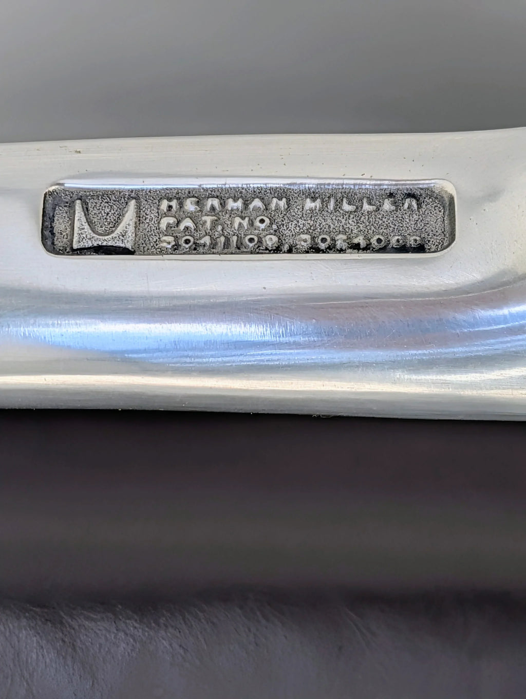 Herman Miller metal label with logo and catalog number on brushed aluminum chair frame