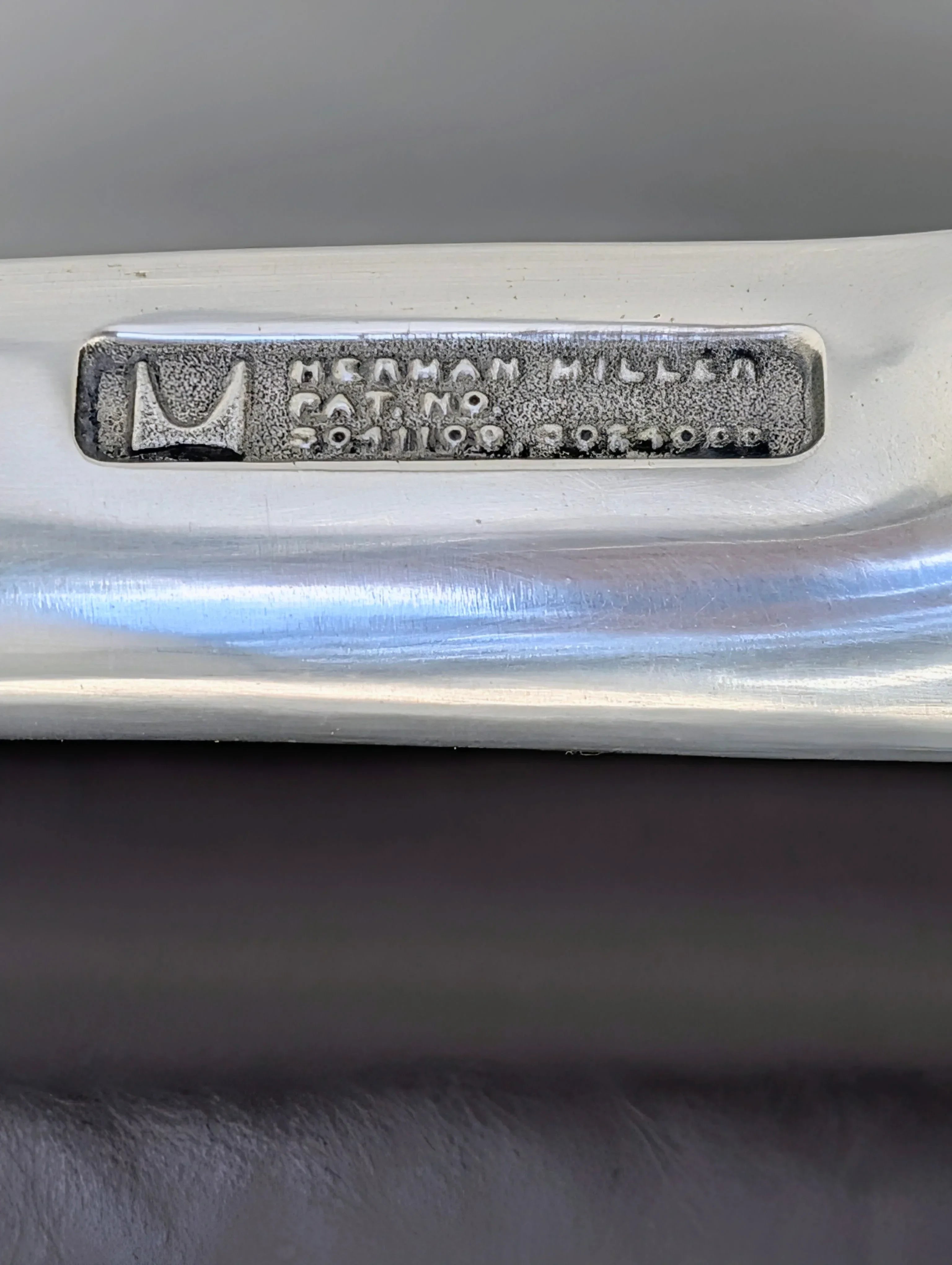 Herman Miller metal label with logo and catalog number on brushed aluminum chair frame