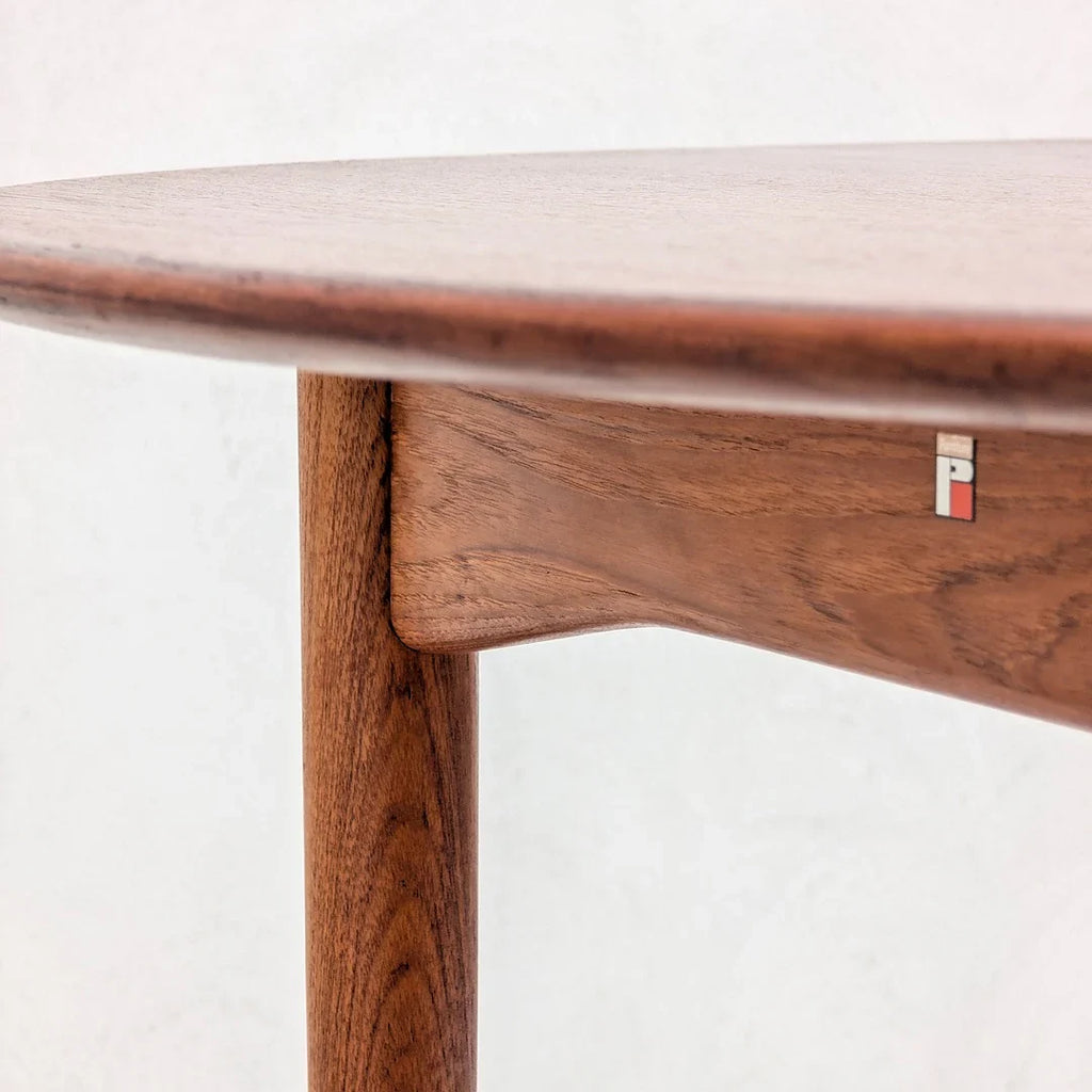 Close-up of mid-century modern round walnut wood table with leg and logo detail