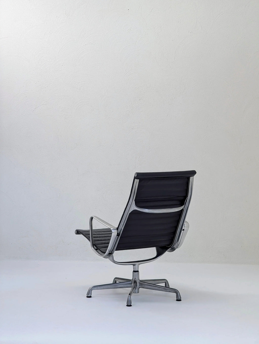 Modern black office chair with metal frame on white floor against a plain textured wall