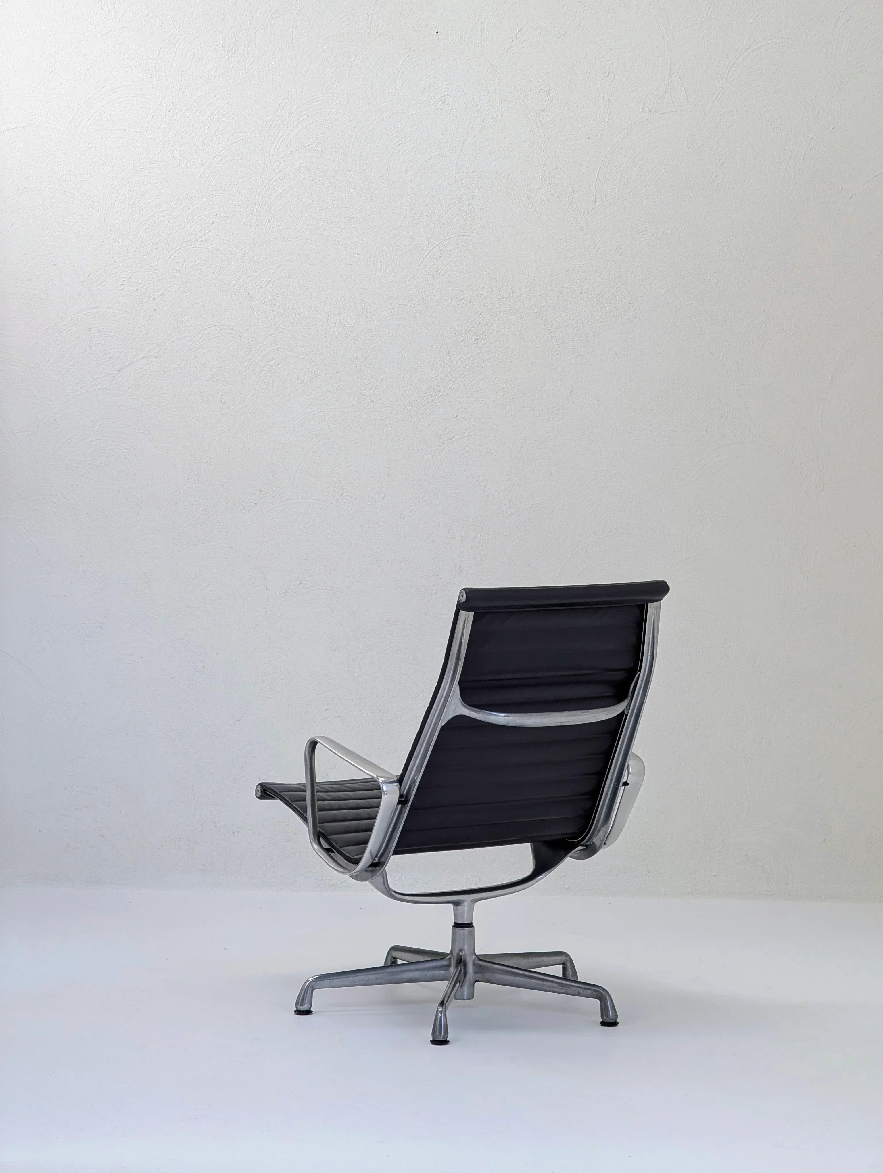 Modern black office chair with metal frame on white floor against a plain textured wall