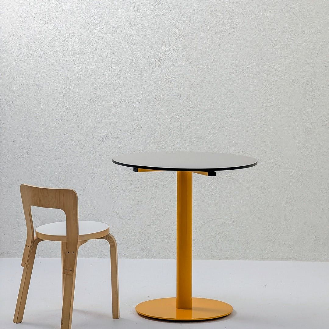 Modern round table with yellow base and wooden chair against white textured wall