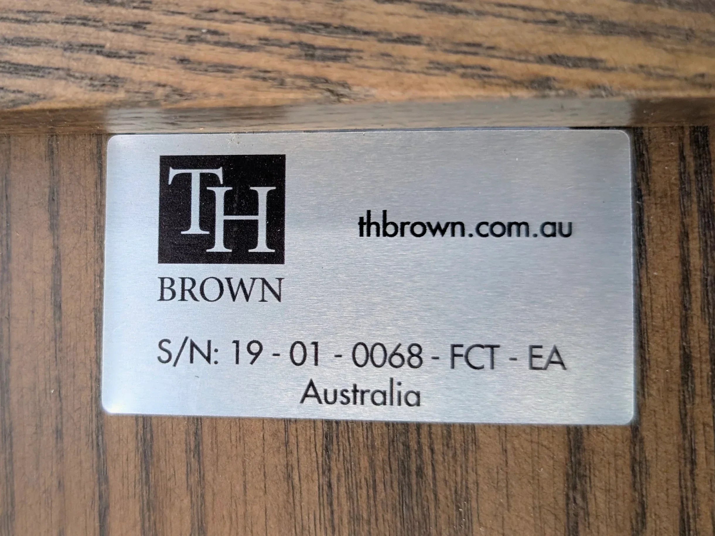 TH Brown metal label with website and serial number on wood furniture surface, Australia
