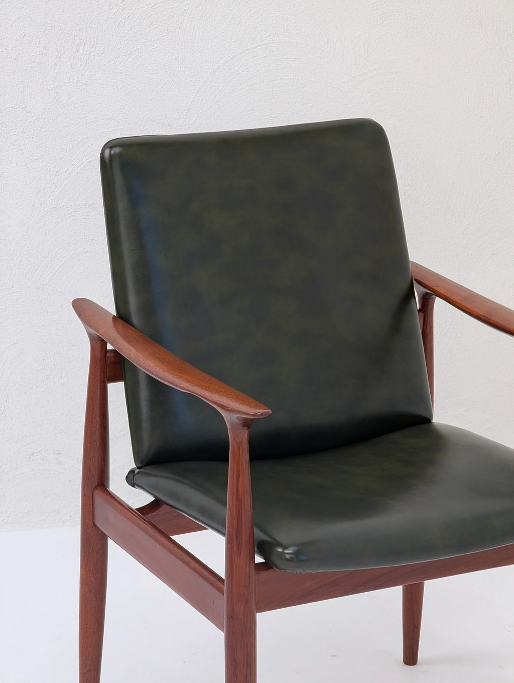 Mid-century modern chair with dark green leather seat and wooden frame against white wall