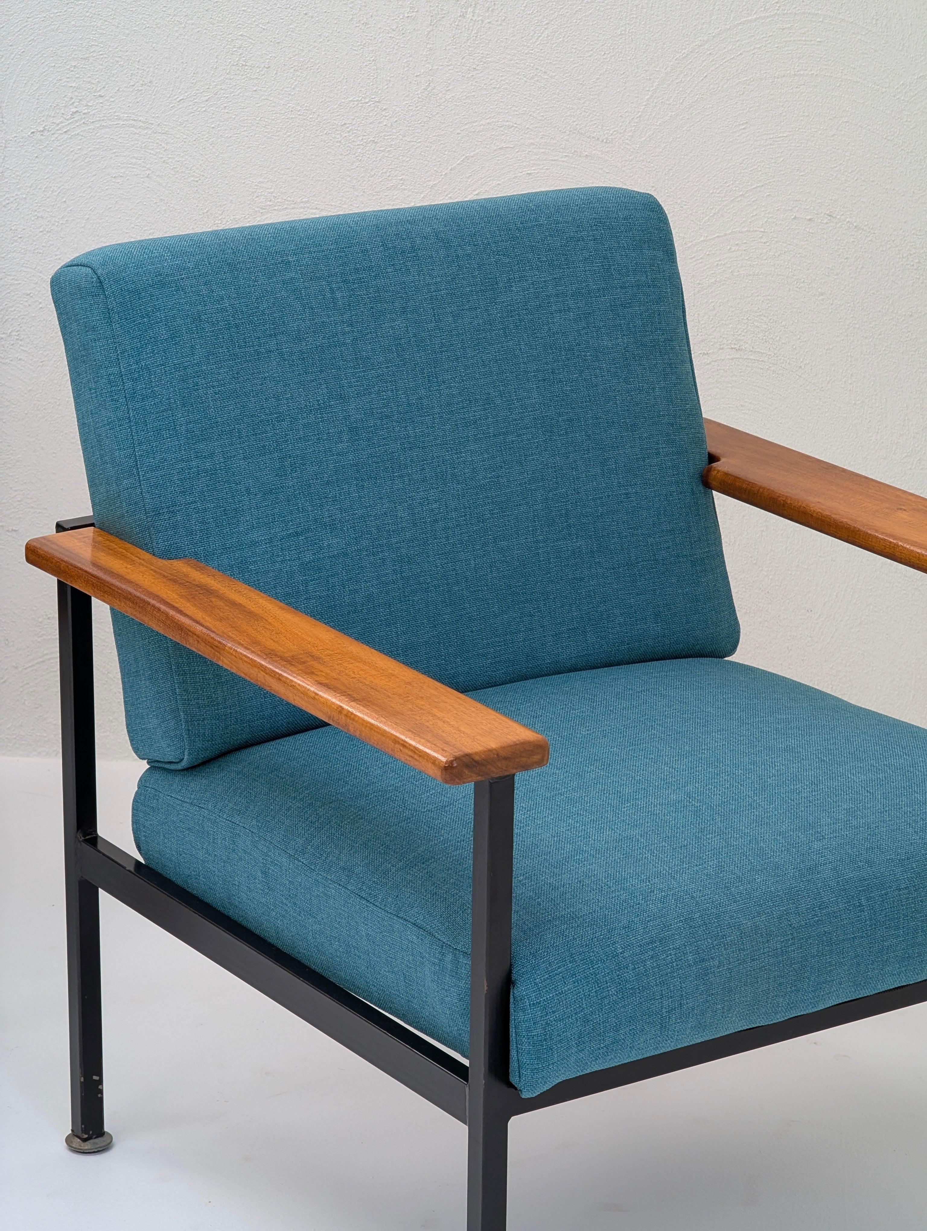 Modern armchair with teal fabric, wood armrests, and black metal frame against white wall