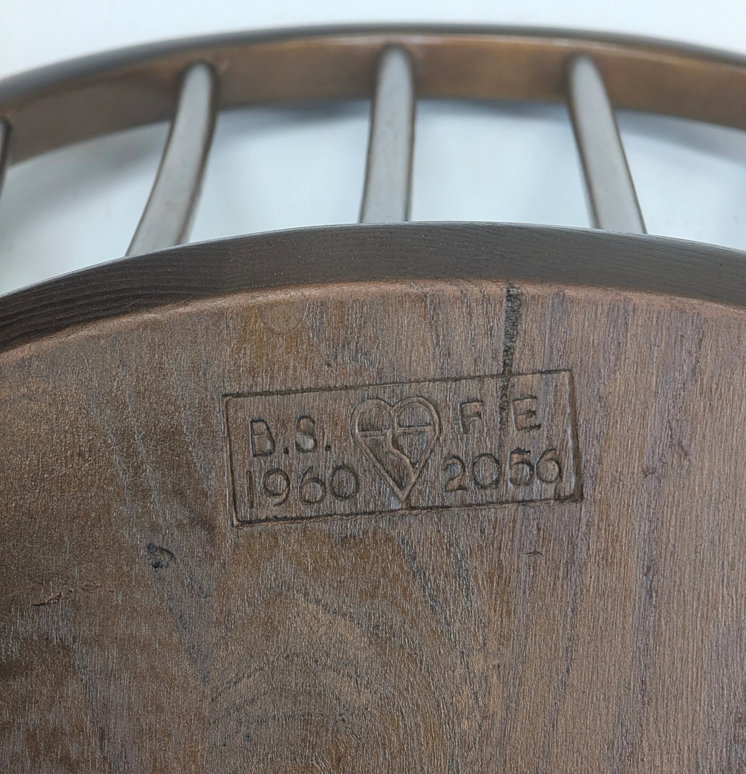 Close-up of wooden chair backrest with carved stamp featuring heart and text D.S. 1960 F.E. 2056