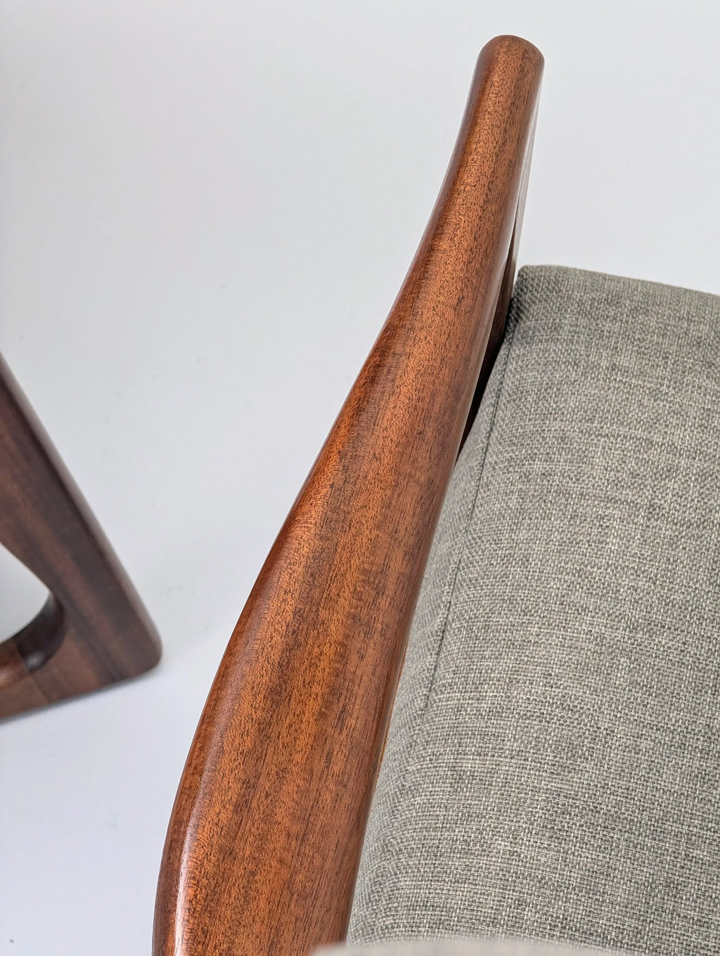 Close-up of a modern chair with curved walnut wood armrest and grey fabric upholstery
