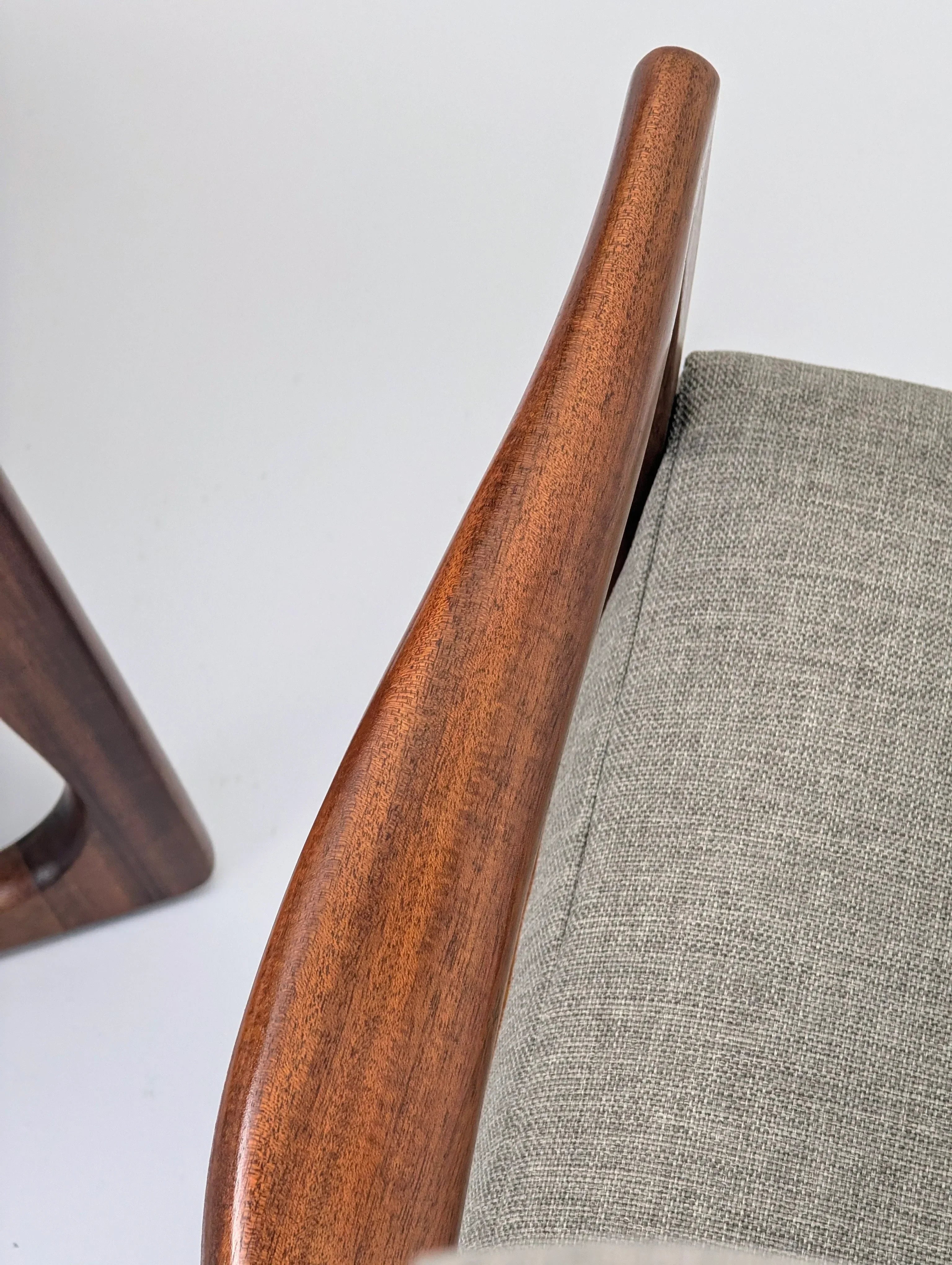 Close-up of a modern chair with curved walnut wood armrest and grey fabric upholstery