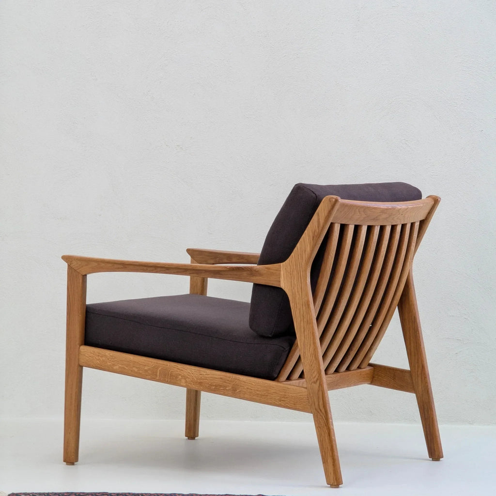 Mid-century modern wooden accent chair with dark cushions and slatted back on white background