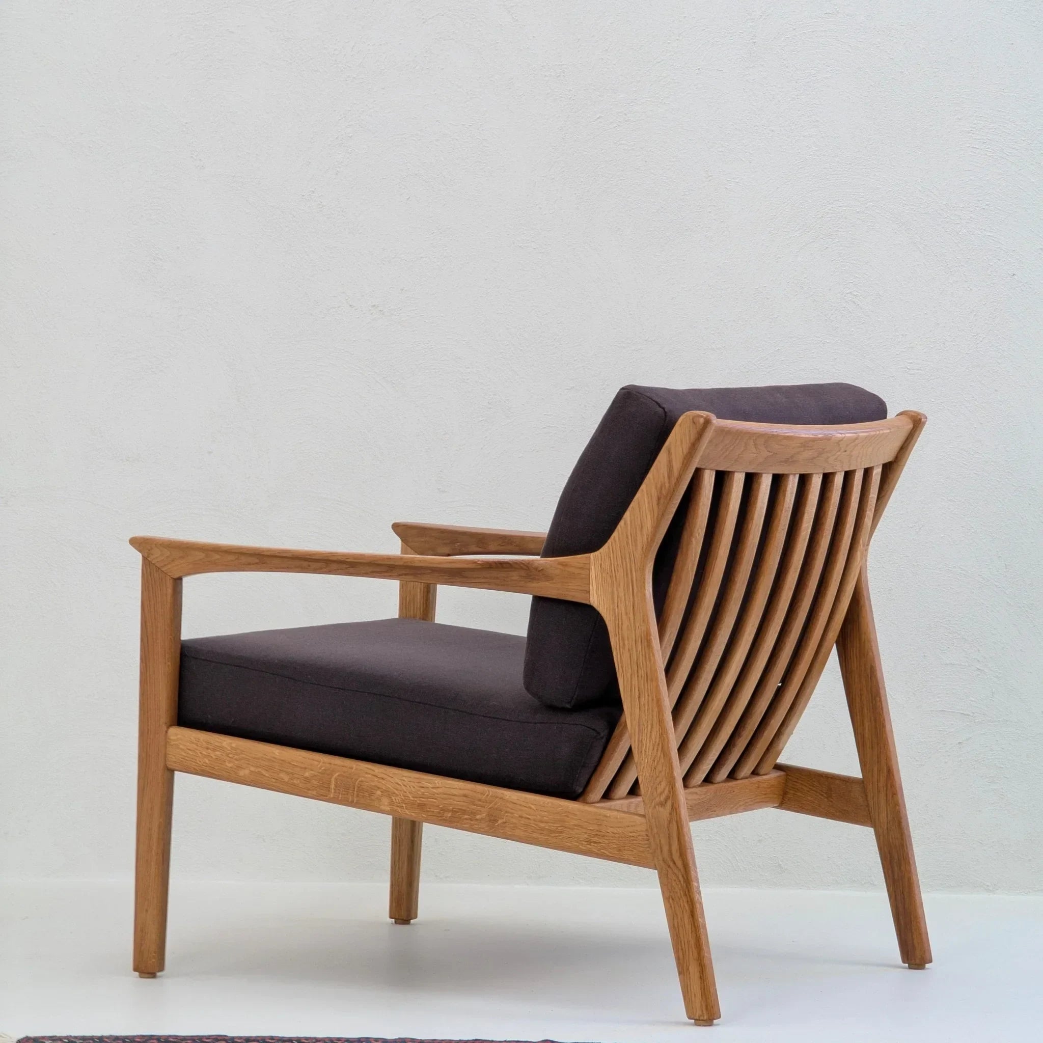 Mid-century modern wooden accent chair with dark cushions and slatted back on white background