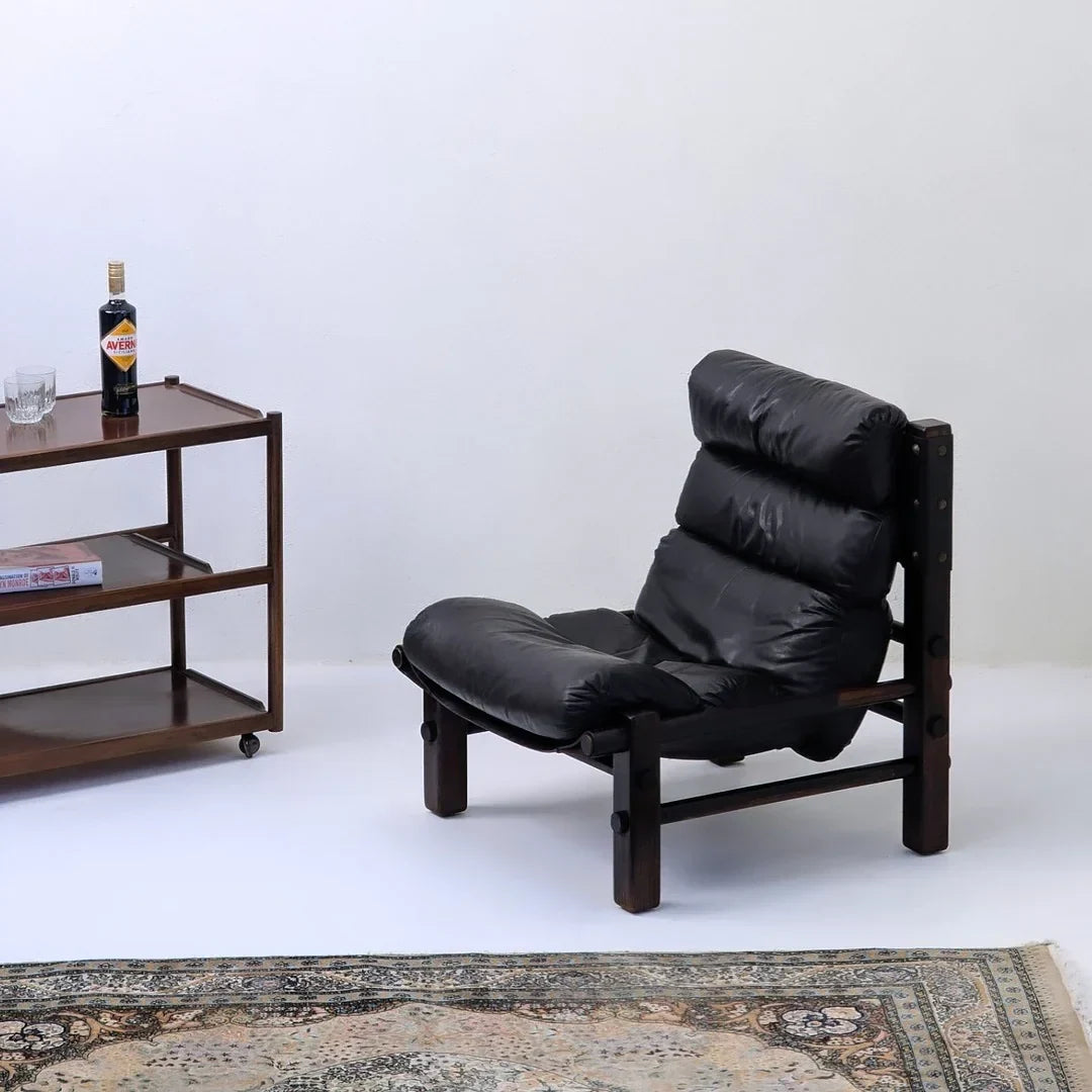 Vintage black leather lounge chair with wooden frame, bar cart, and patterned rug in minimalist room