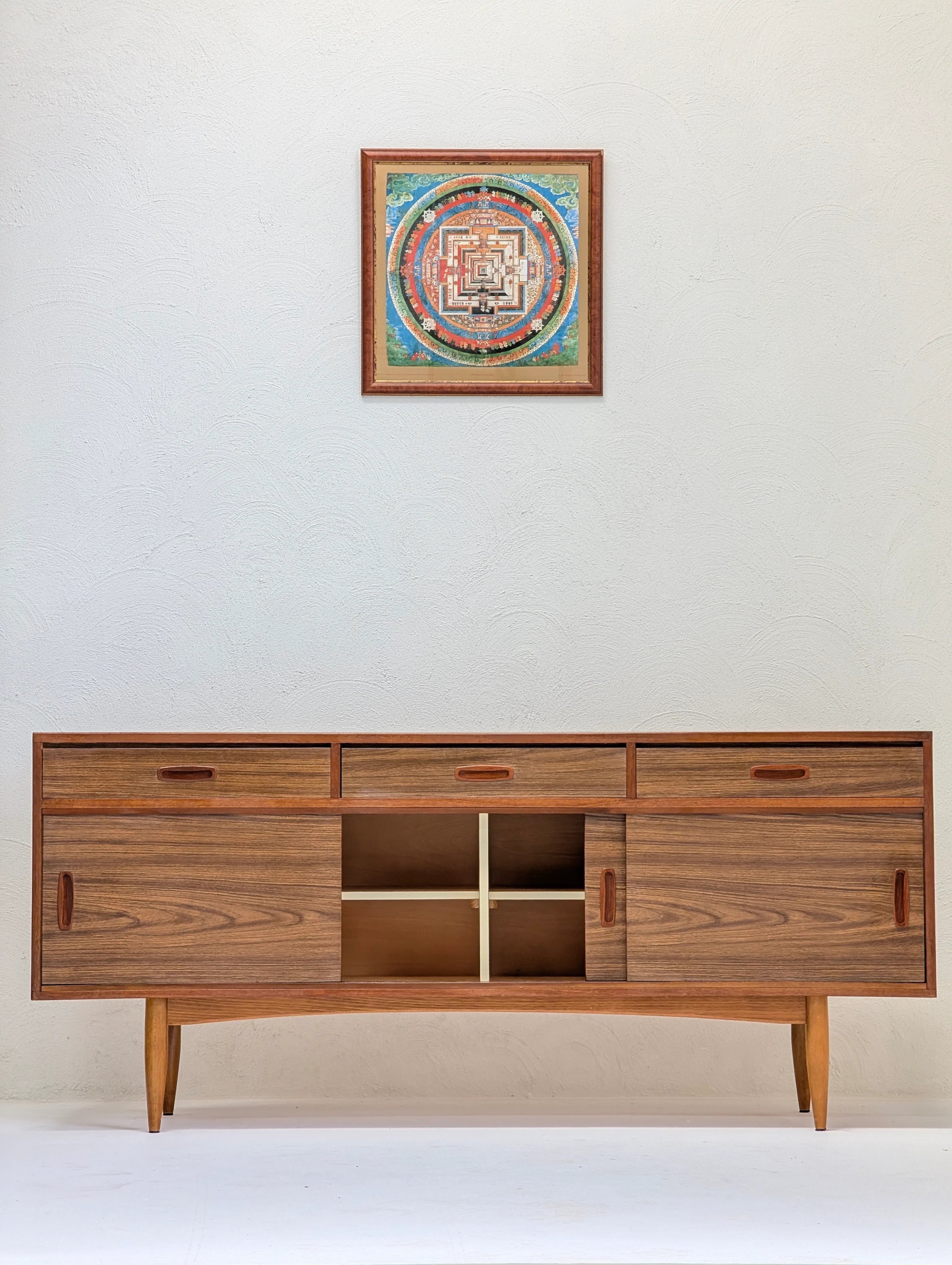 Mid-century modern wooden credenza with sliding doors and drawers against textured white wall