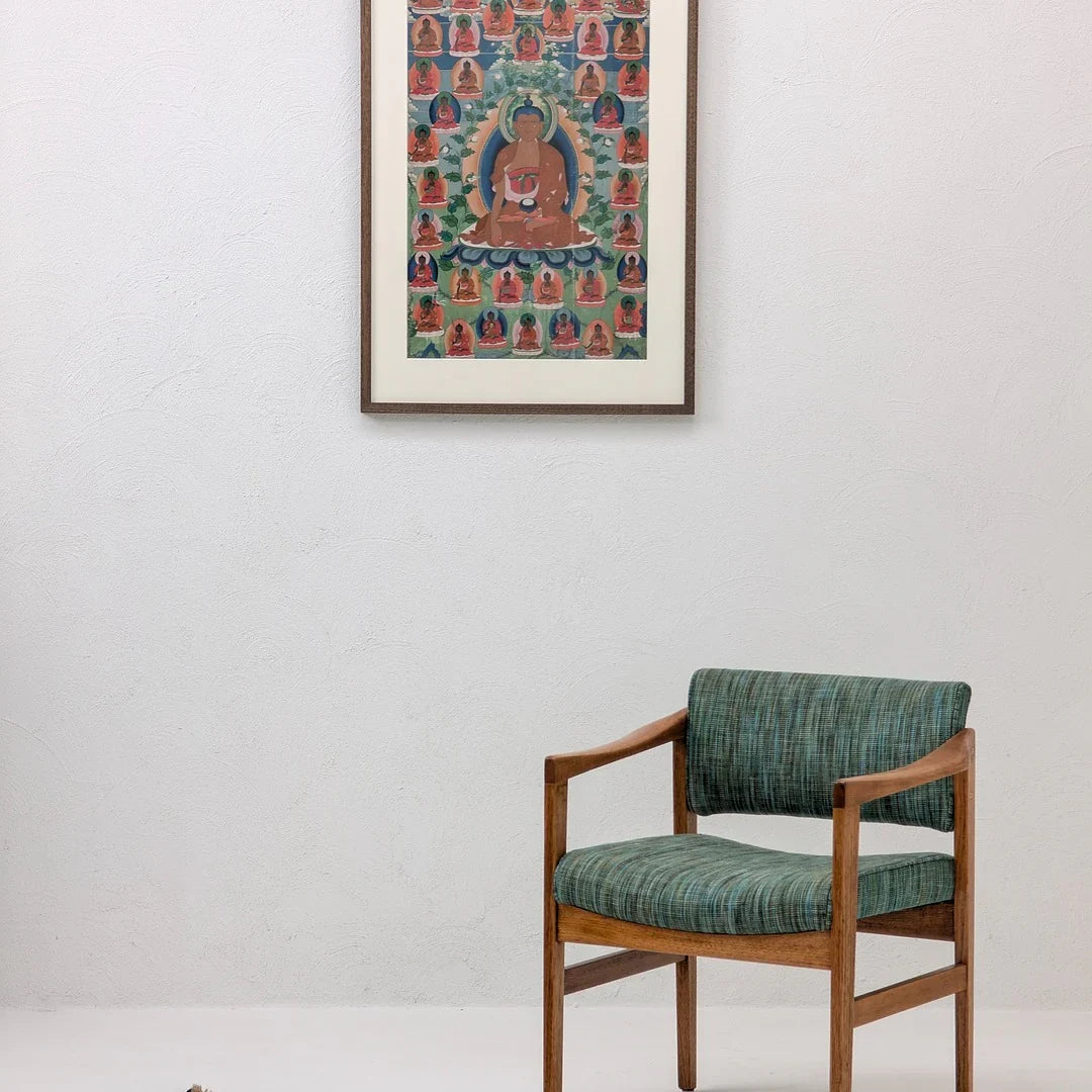 Mid-century modern chair with green upholstery beside framed Buddha art on white wall
