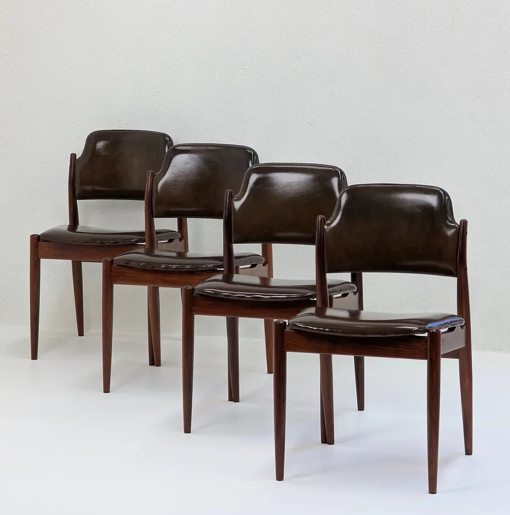 Set of four vintage dark brown leather dining chairs with wooden legs against a light wall