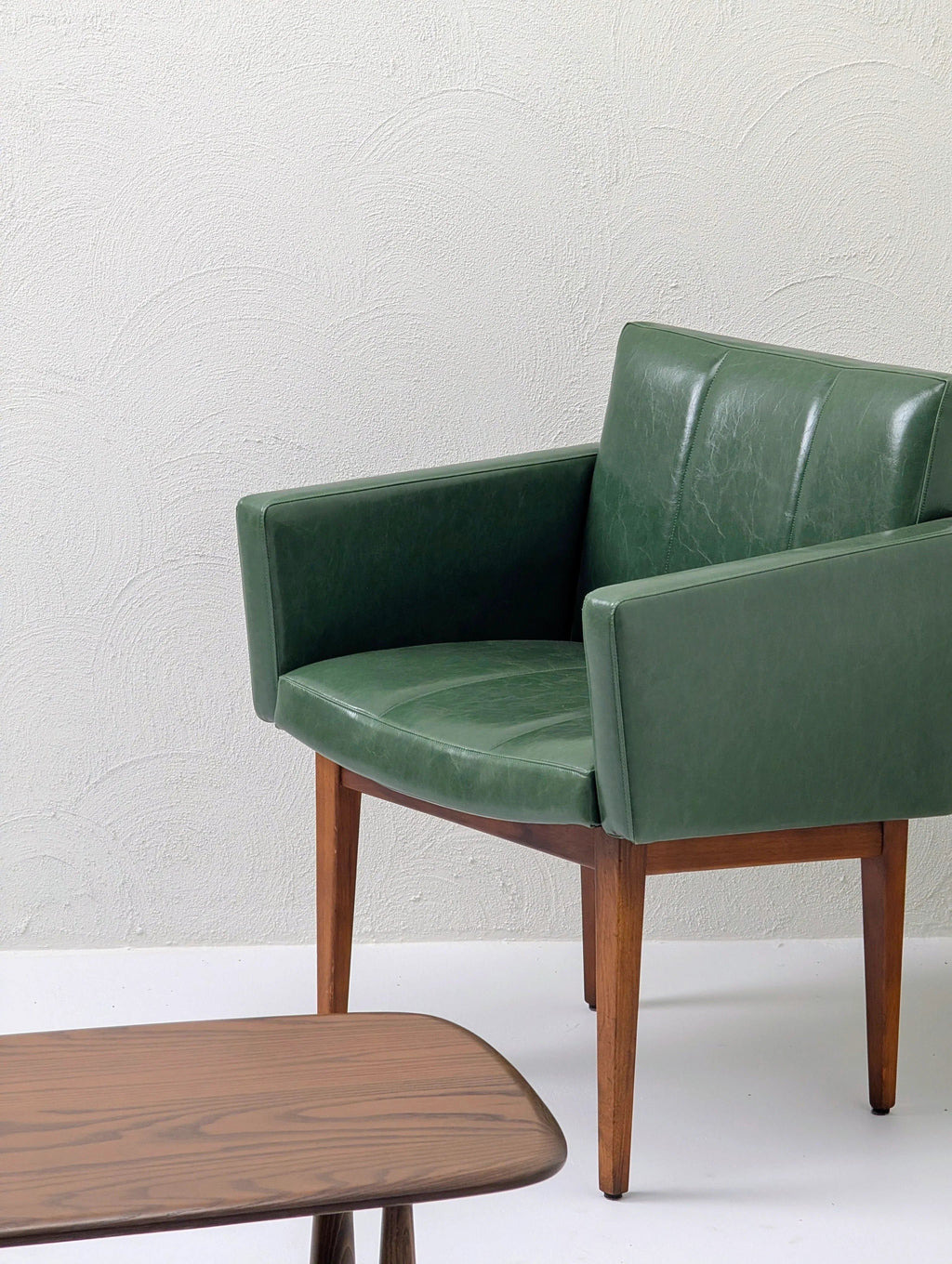 Mid-century modern green leather armchair with wooden legs next to a wooden coffee table