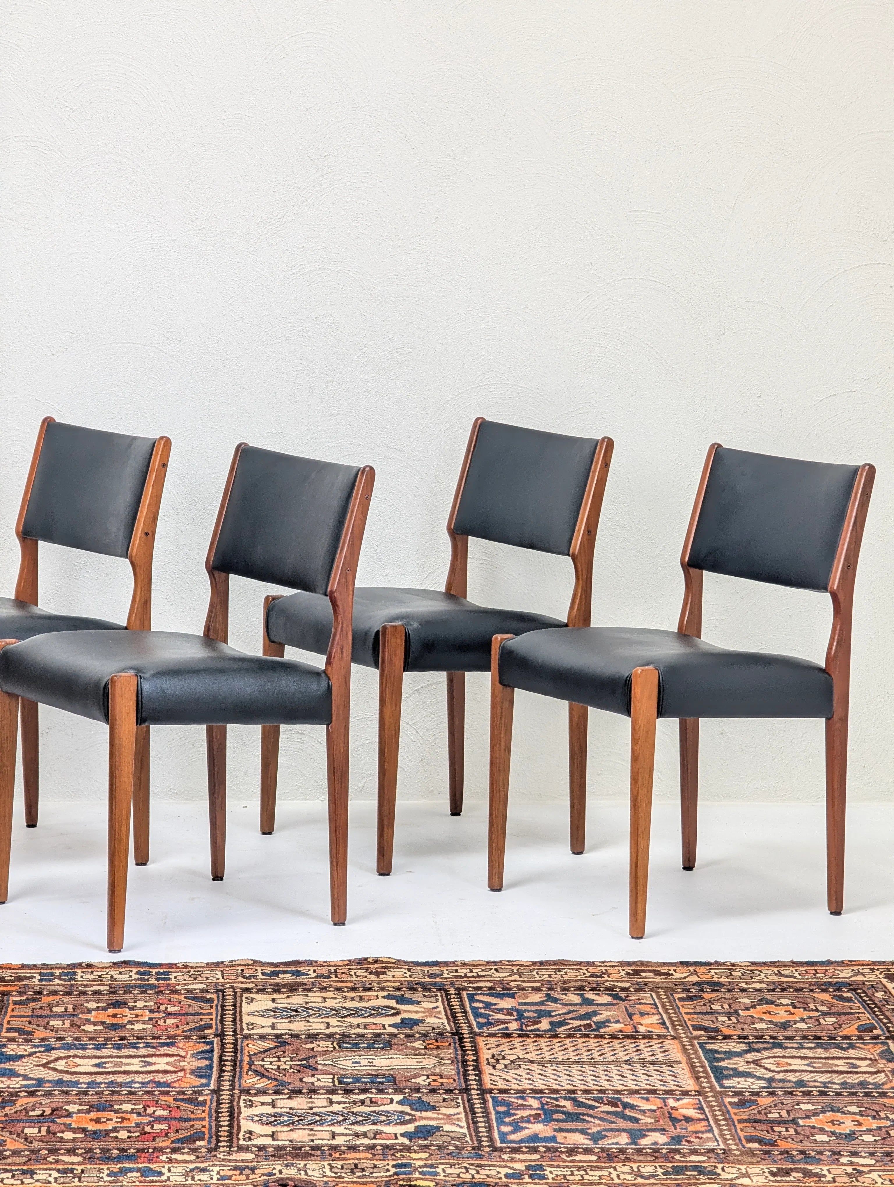 Set of four mid-century modern wooden chairs with black leather seats and backs on a patterned rug