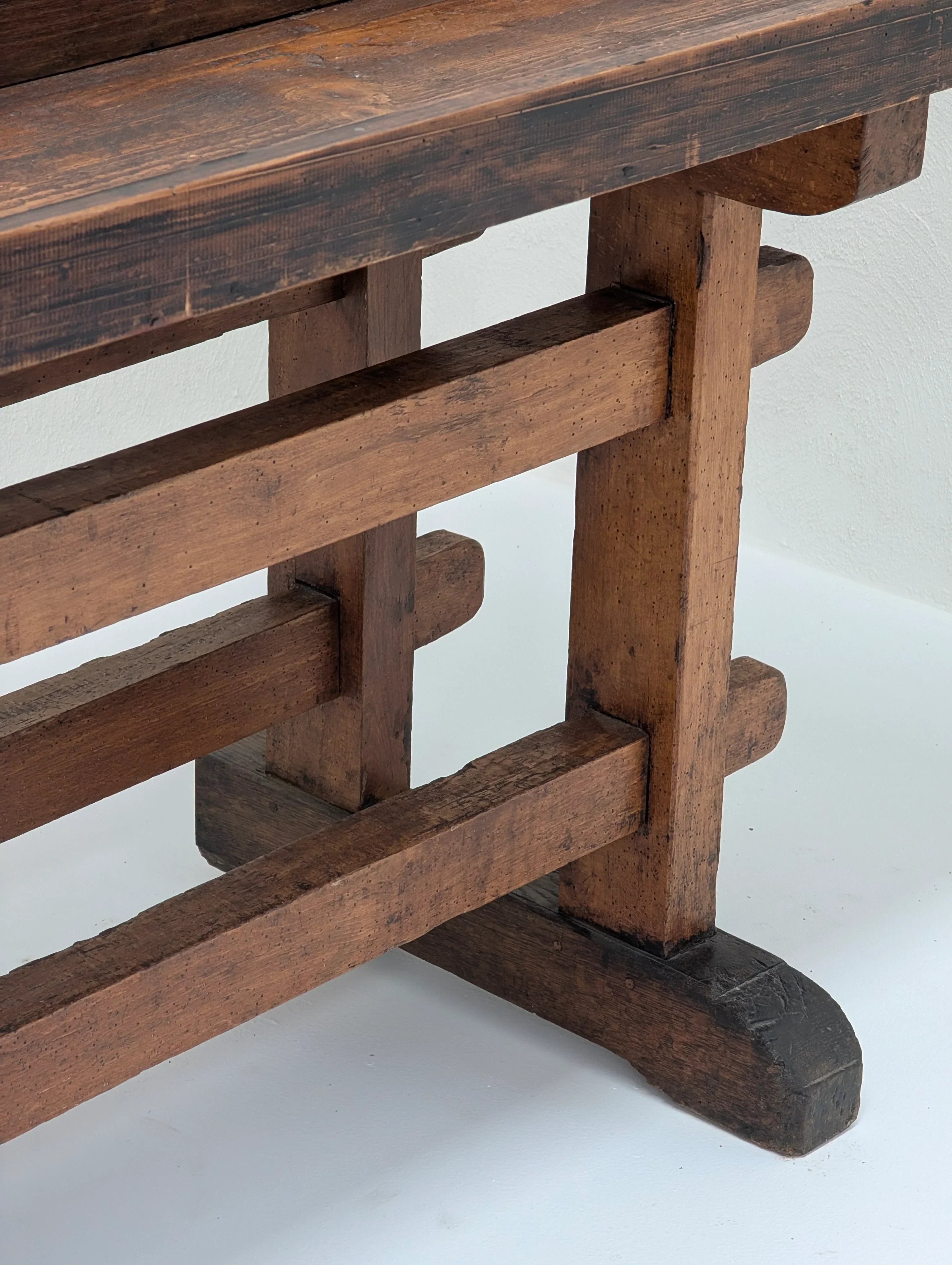 Close-up of rustic wooden bench legs and frame against a white wall and floor
