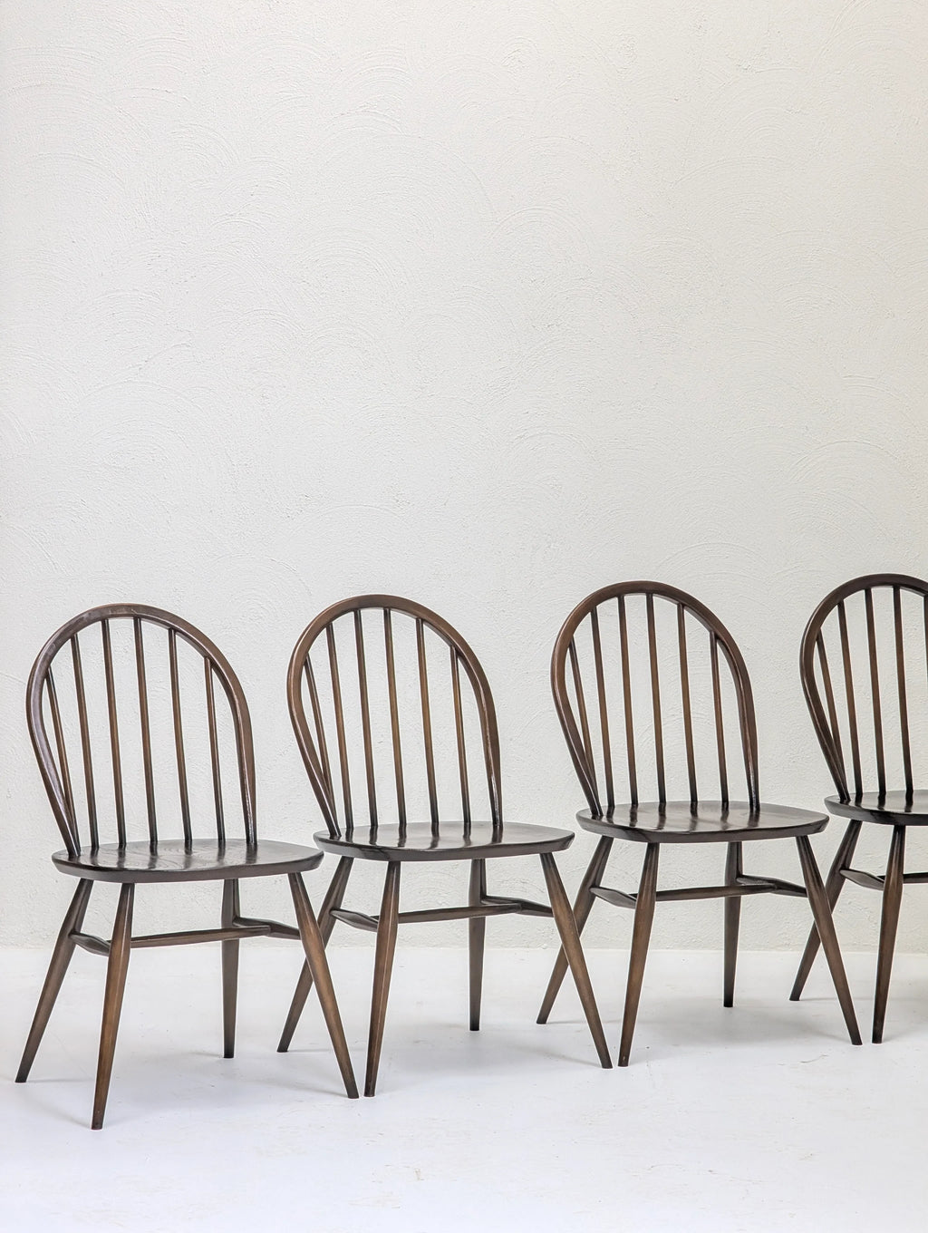 Four dark wooden spindle-back dining chairs against a white textured wall