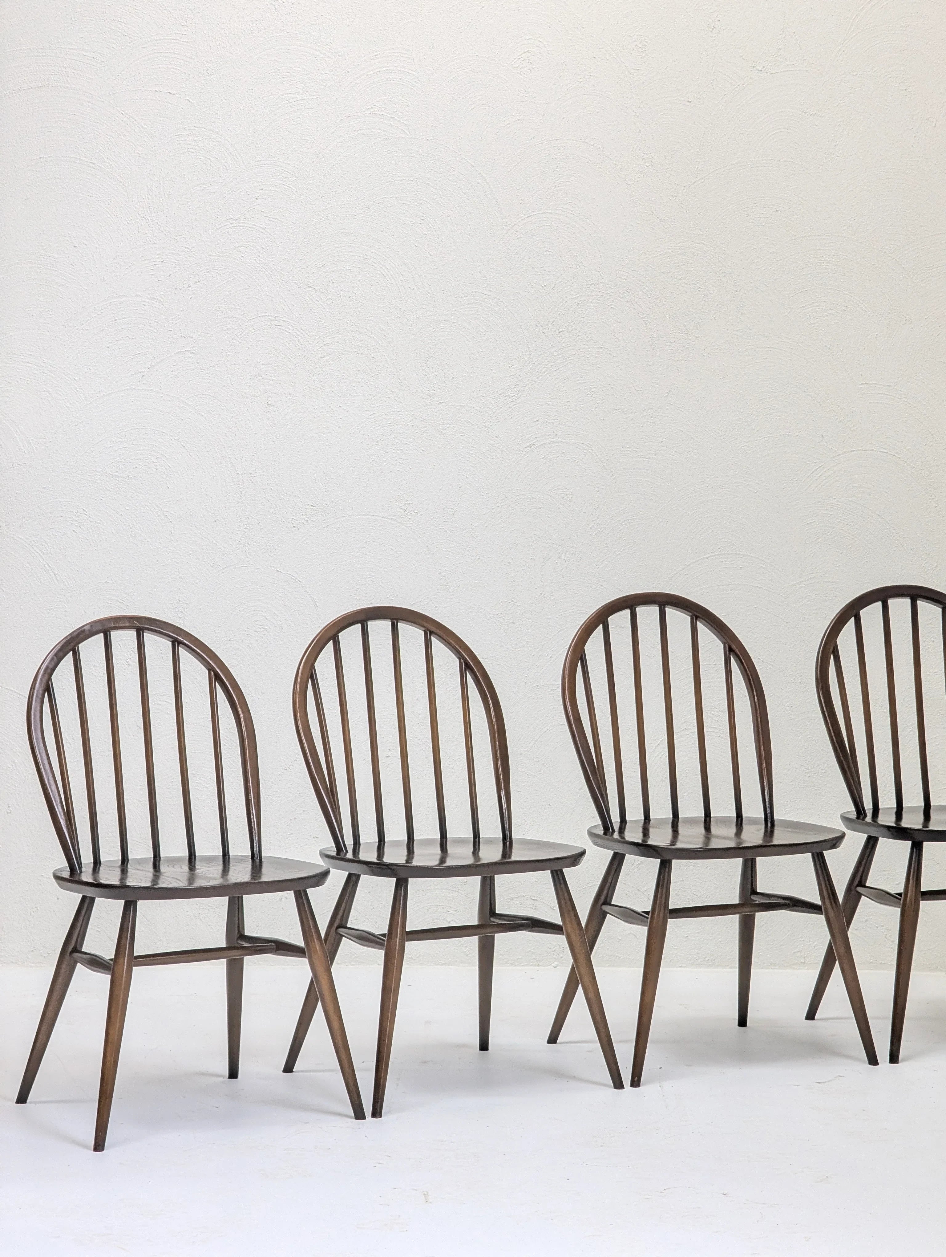 Four dark wooden spindle-back dining chairs against a white textured wall
