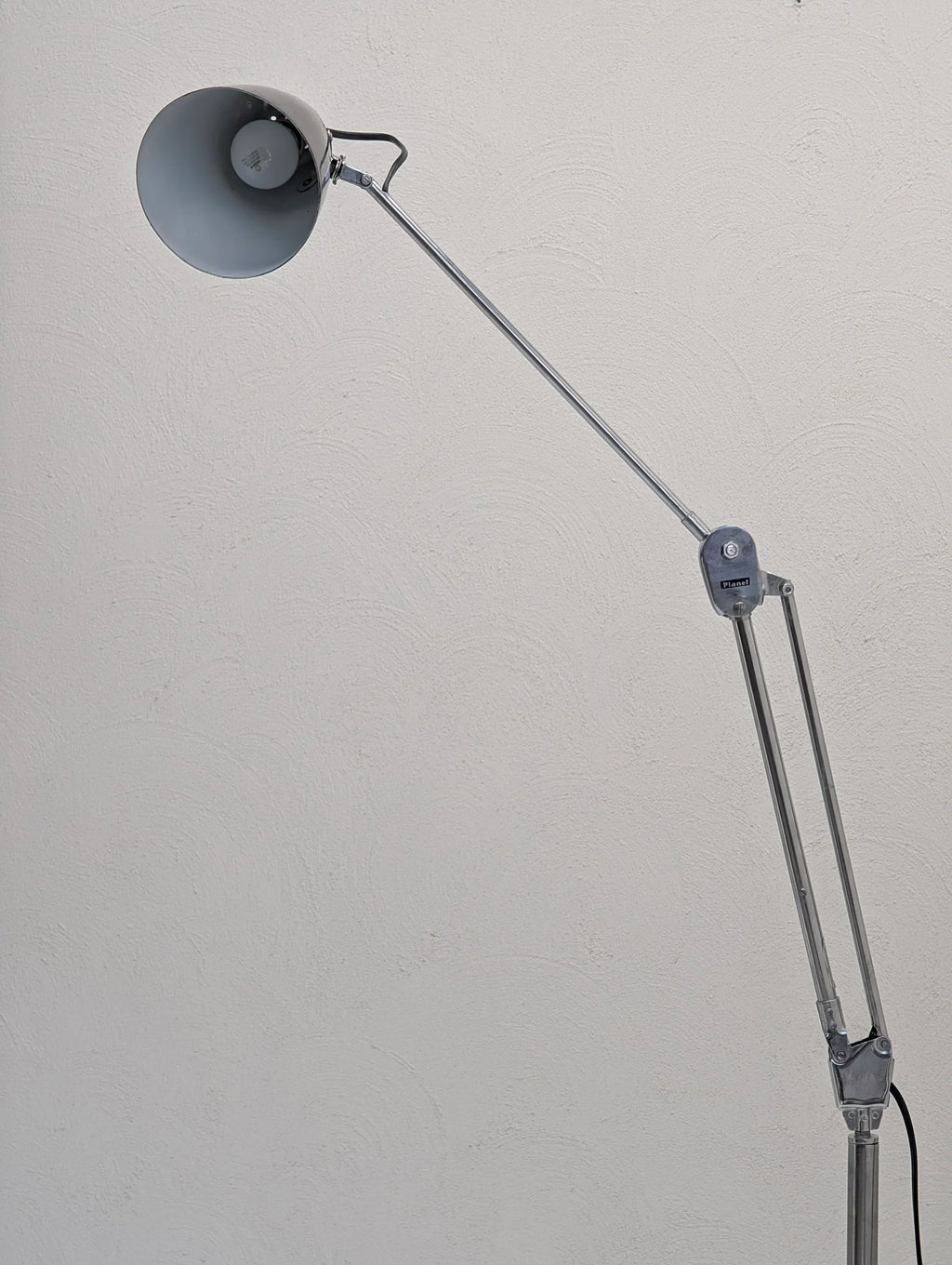 Modern adjustable desk lamp with metal arm against textured white wall