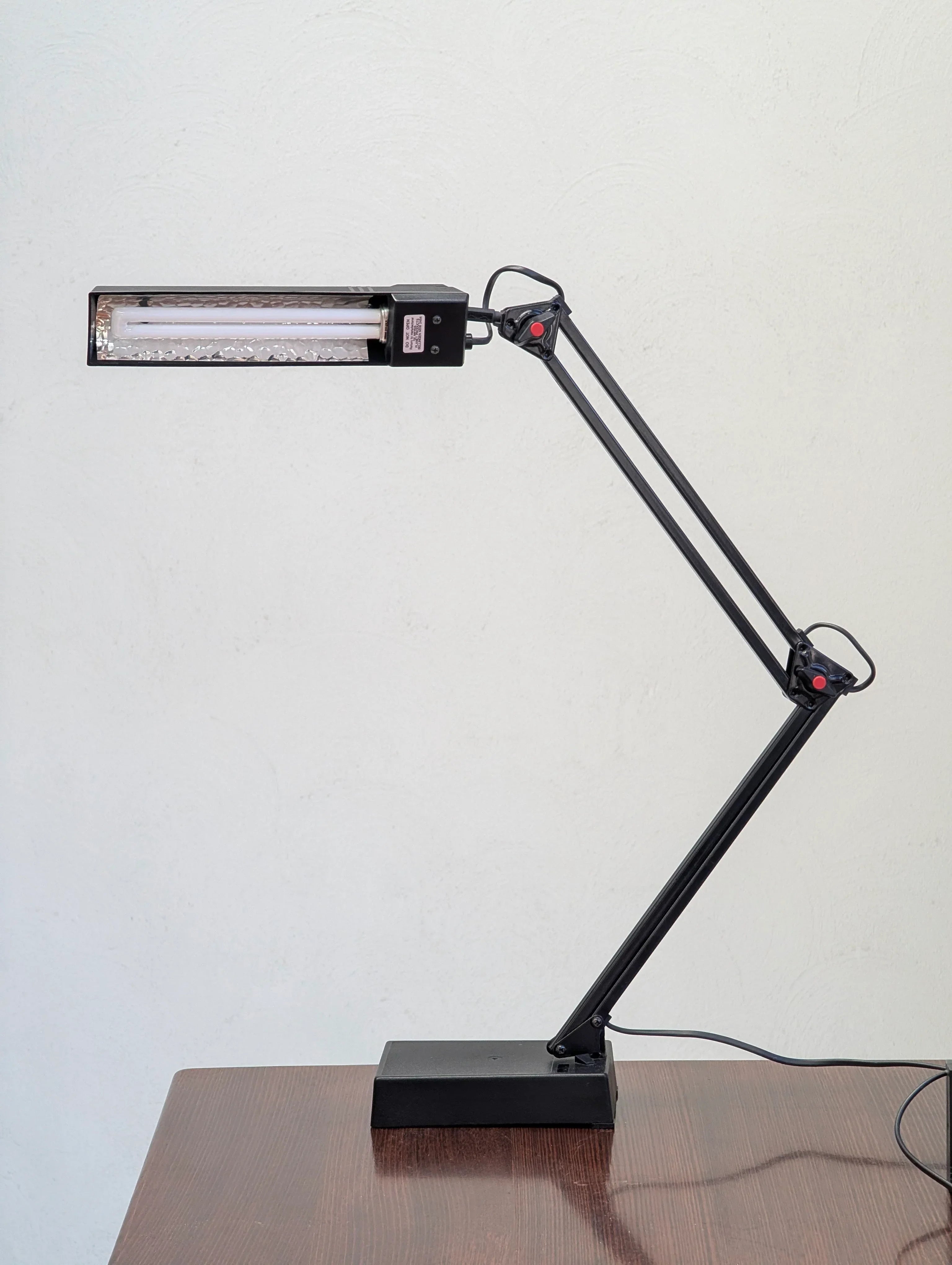 Black adjustable desk lamp with fluorescent tube on a wooden table against a white wall