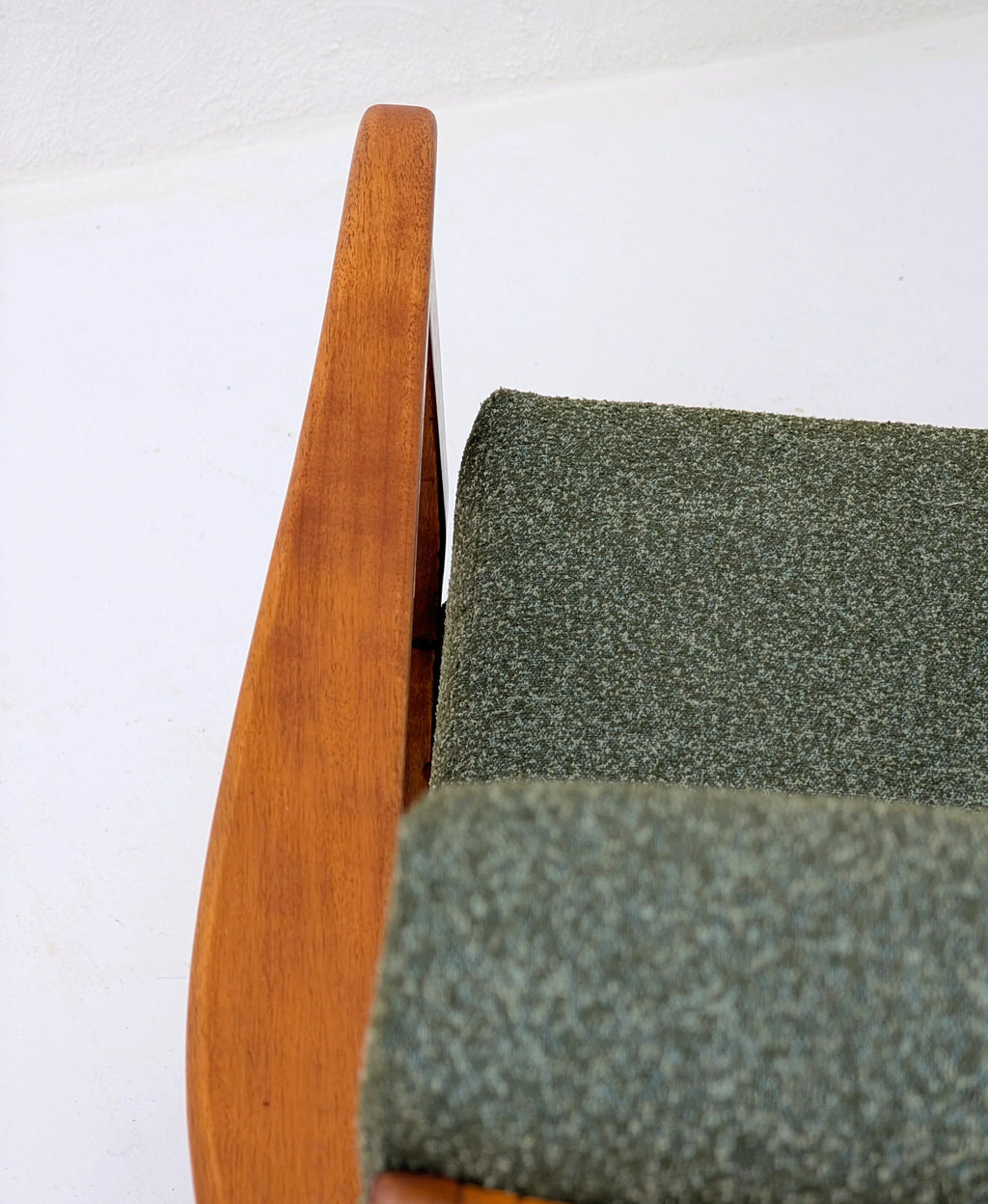 Close-up of mid-century modern chair with green textured fabric and wooden armrest on white background