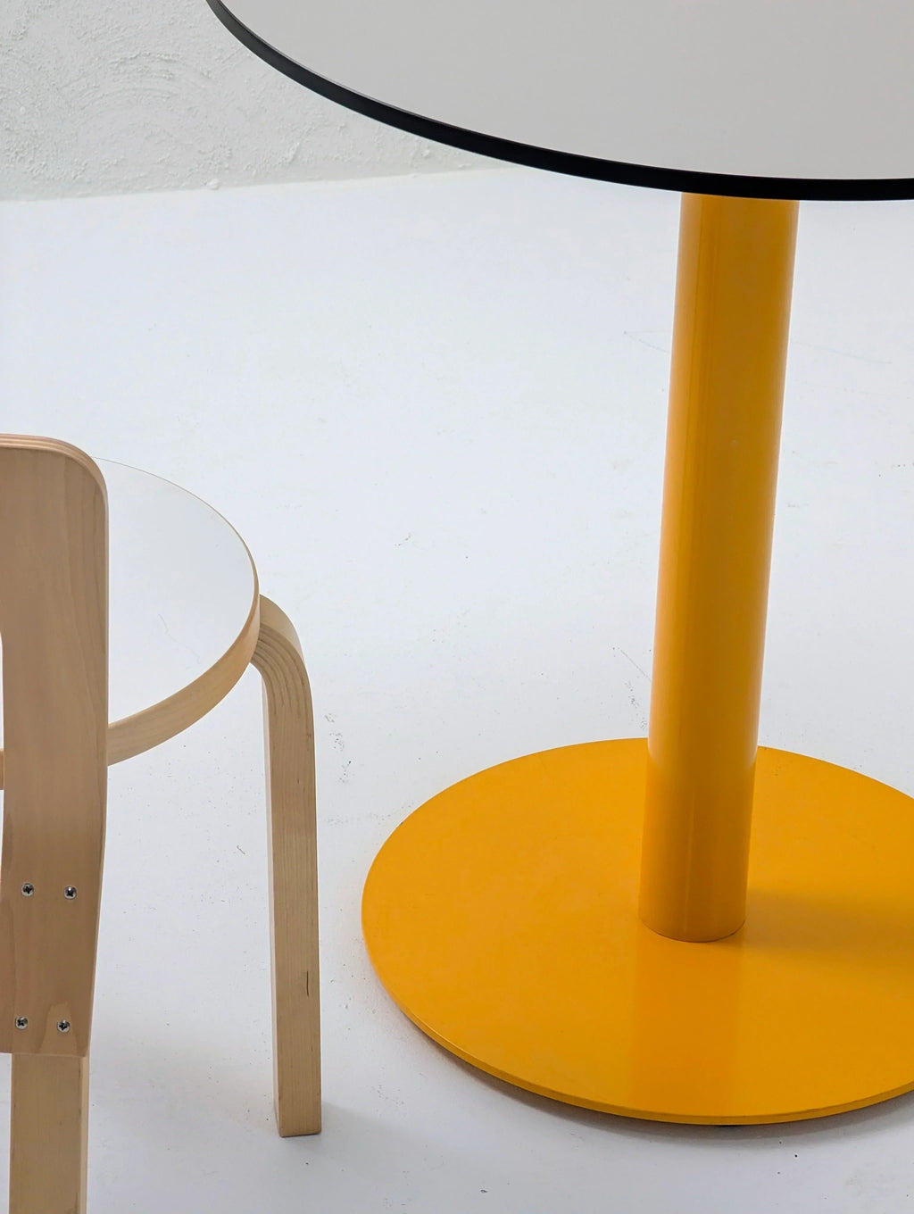 Modern round table with yellow base and light wood chair in minimalist setting