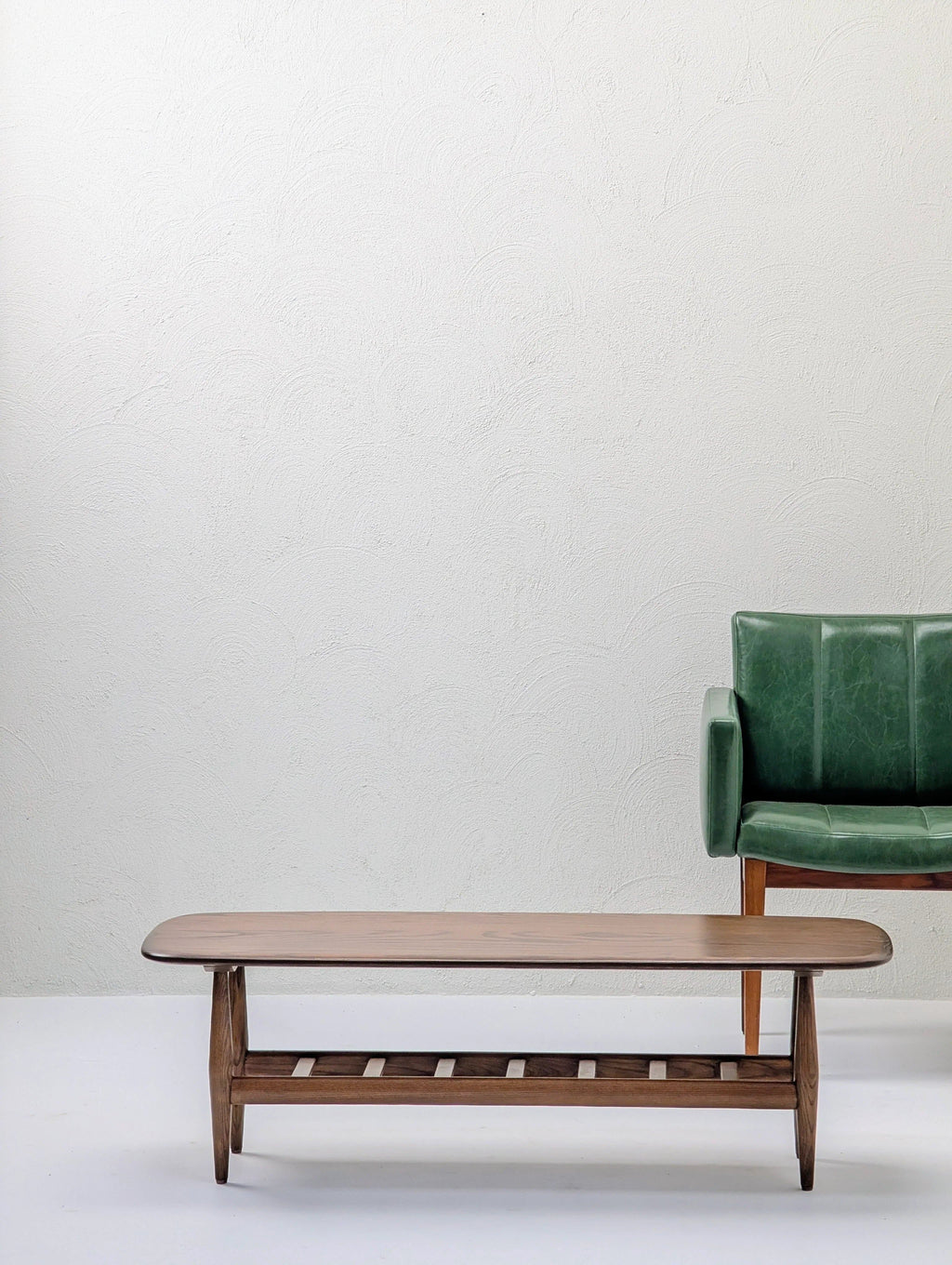 Minimalist living room with wooden coffee table and green armchair against white wall