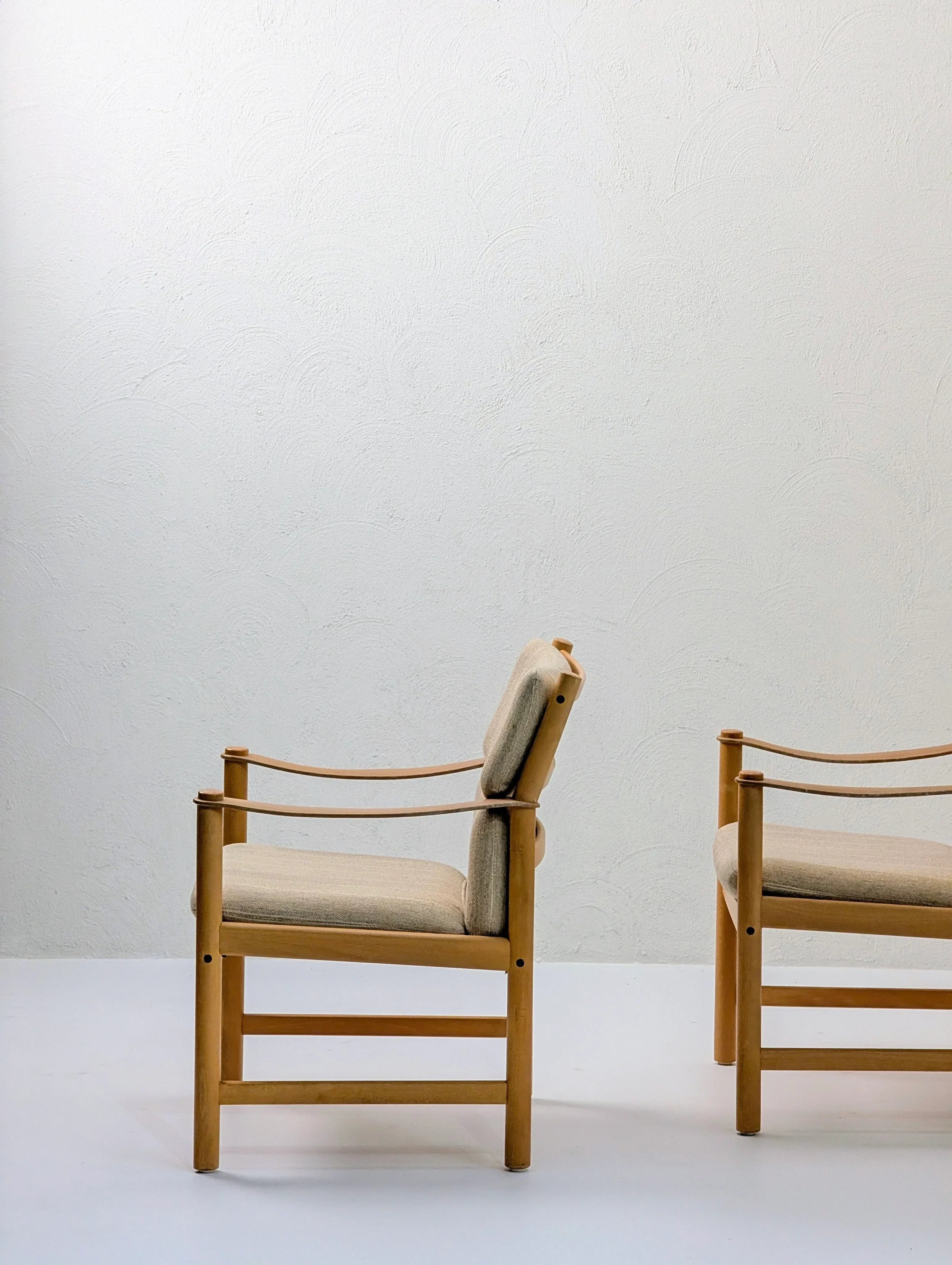 Minimalist wooden chairs with beige cushions against a textured white wall, modern interior design