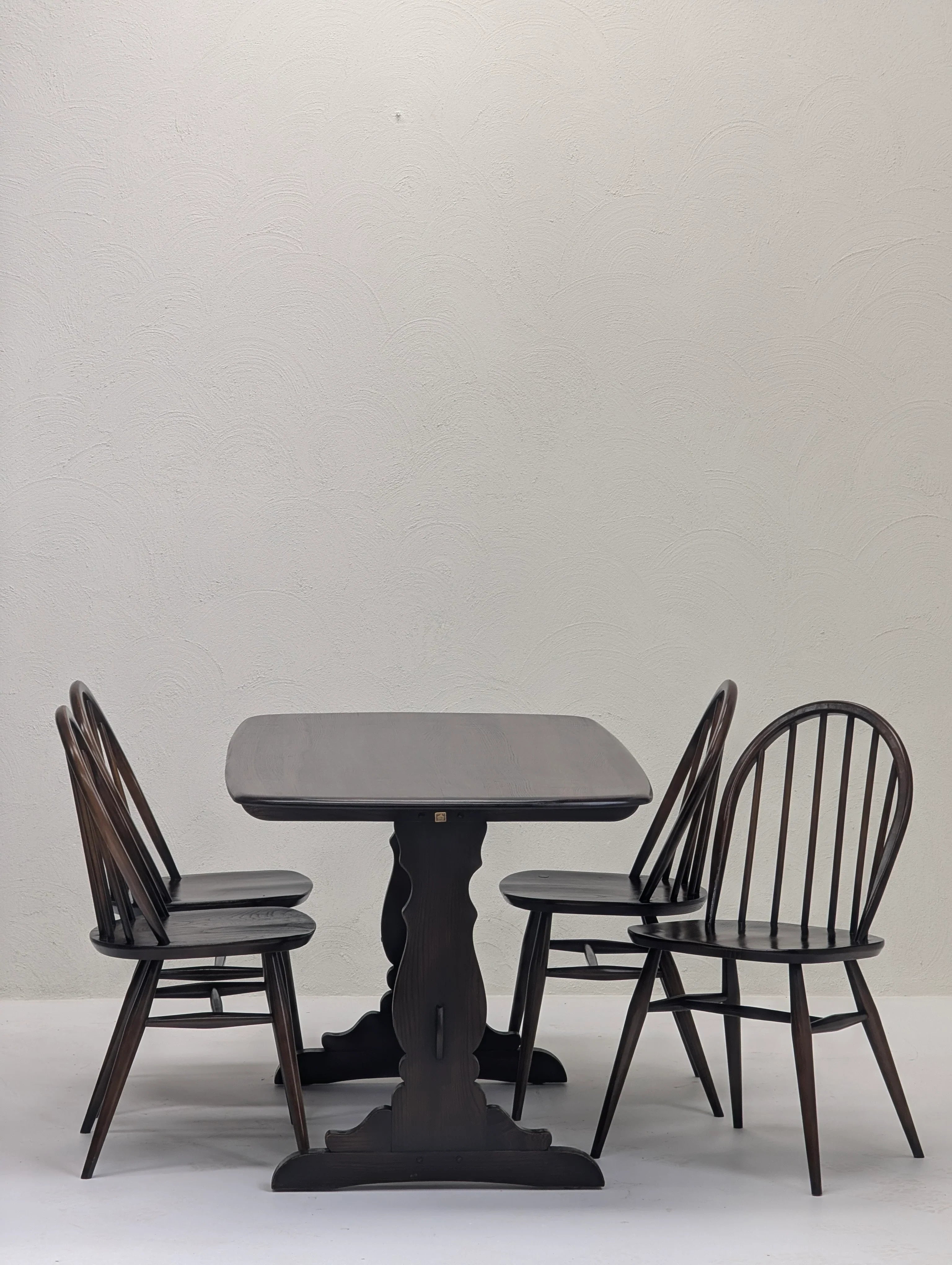Dark wooden dining table with ornate base and four matching spindle-back chairs on white background