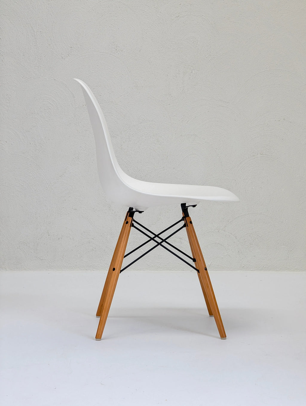 Modern white plastic chair with wooden legs and black metal supports on white floor